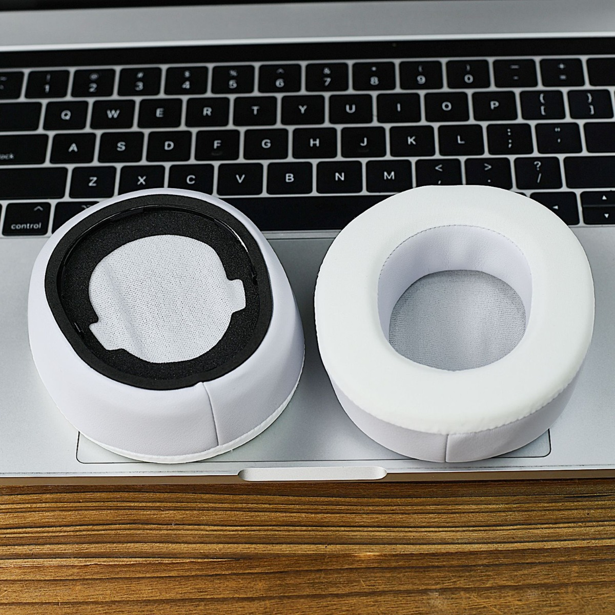 Dos almohadillas blancas para auriculares descansan sobre un teclado de portátil.