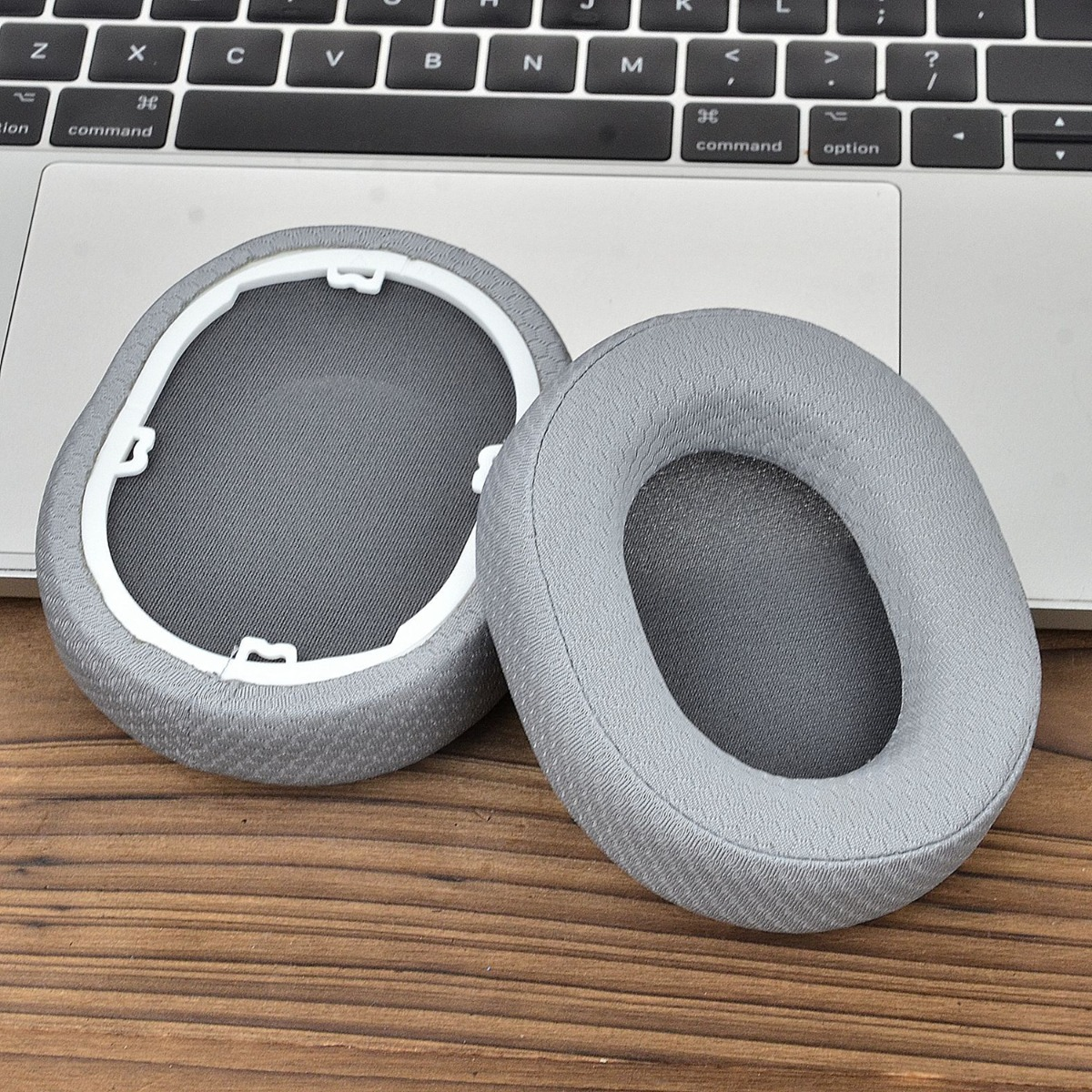 Dos almohadillas grises para auriculares descansan sobre un portátil y mesa.