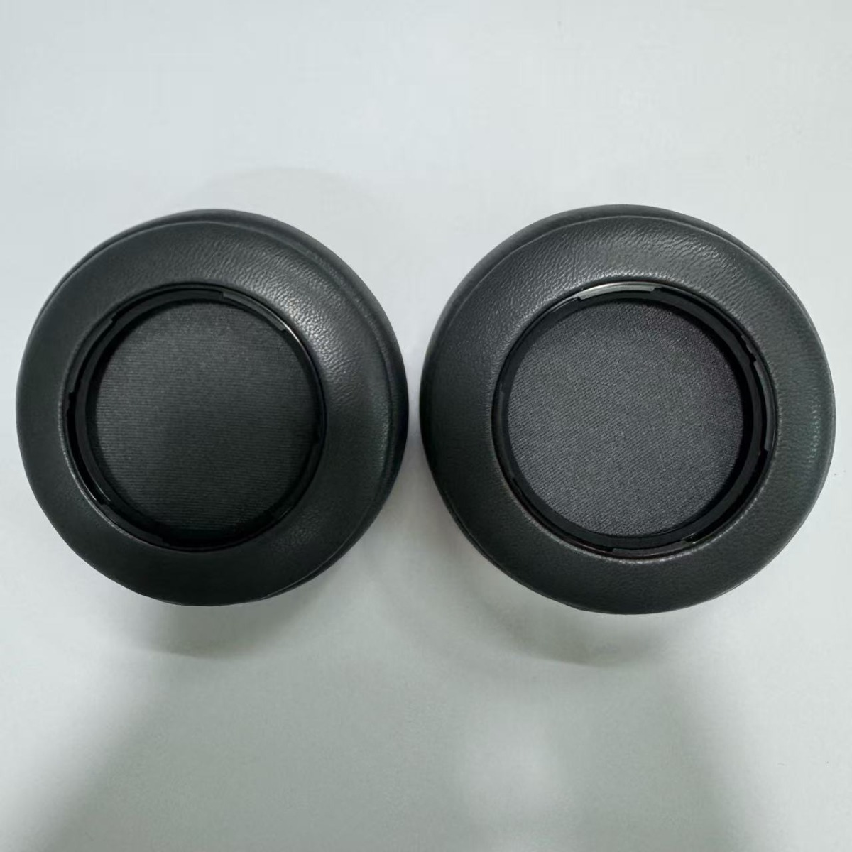 Dos almohadillas negras para auriculares están una al lado de la otra sobre una superficie blanca.