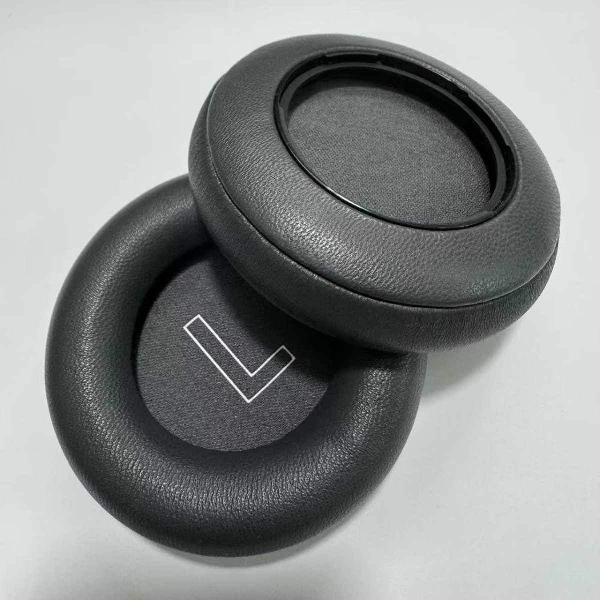 Dos almohadillas negras para auriculares apiladas, una con un símbolo L blanco.