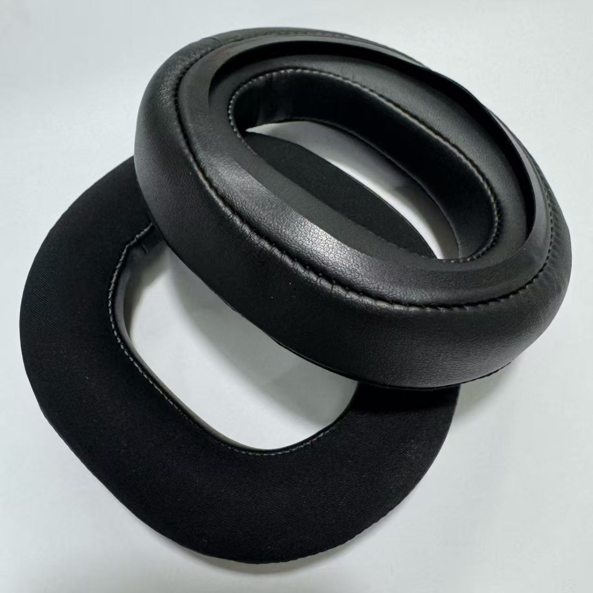 Dos almohadillas negras, una de cuero, otra de tela, sobre fondo blanco.