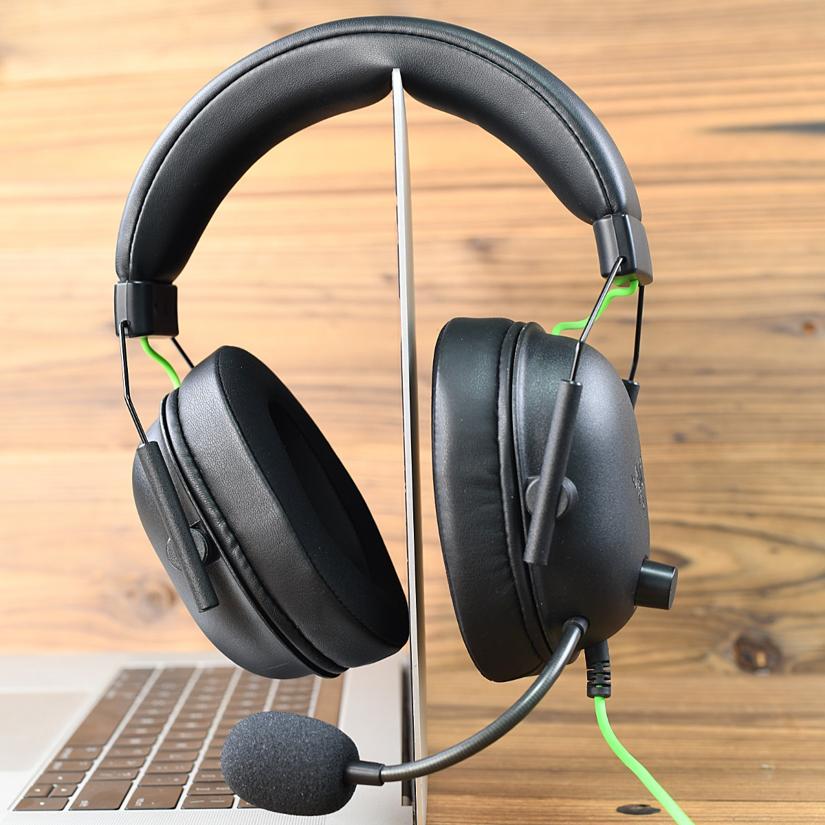 Auriculares negros con micrófono apoyados en un portátil sobre fondo de madera.