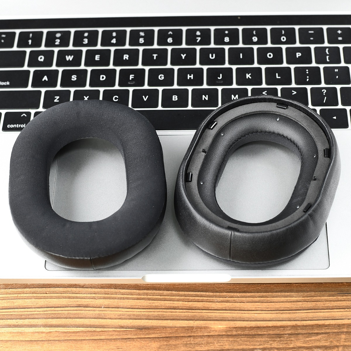 Dos almohadillas negras de auriculares descansan sobre un teclado de portátil.