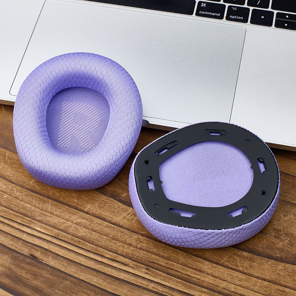 Dos almohadillas moradas para auriculares descansan sobre un portátil y mesa de madera.