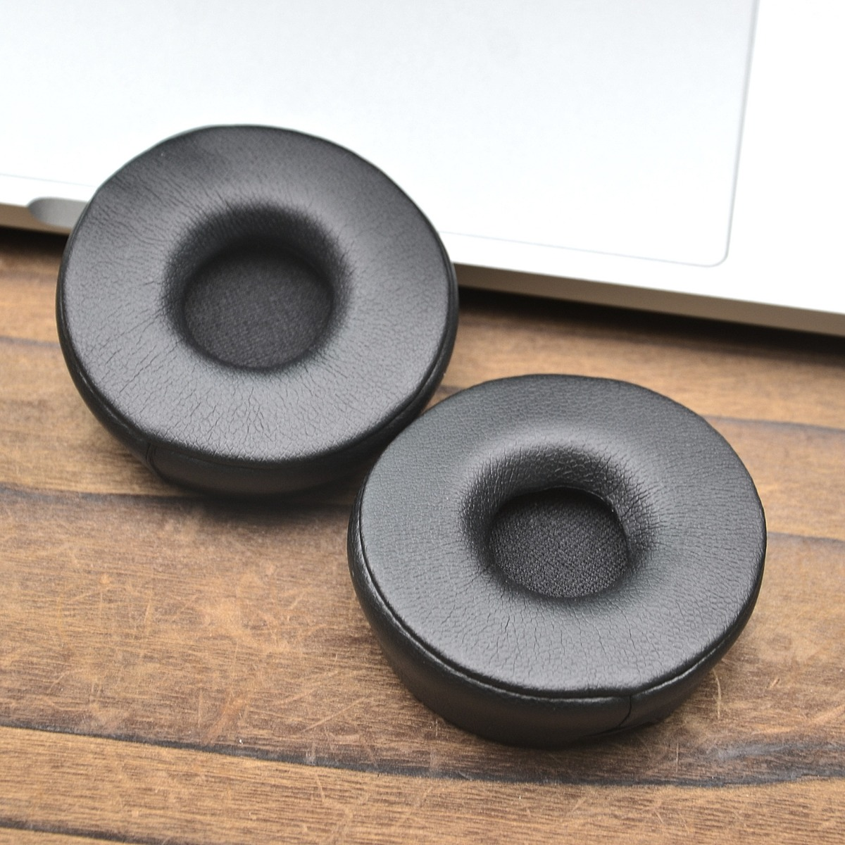 Dos almohadillas negras descansan sobre una mesa de madera junto a un teclado de portátil.