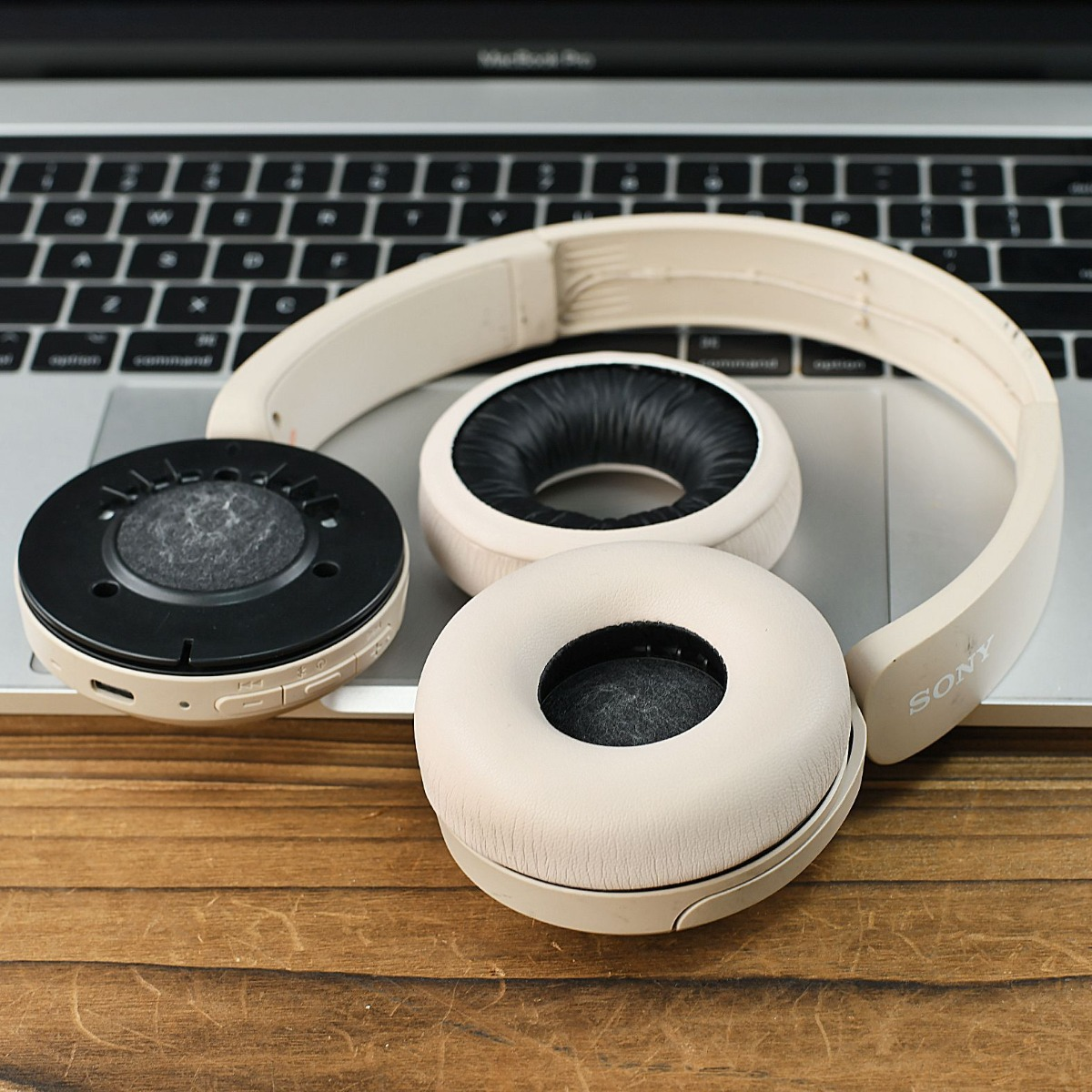 Auriculares Sony beige desmontados sobre un portátil y superficie de madera.