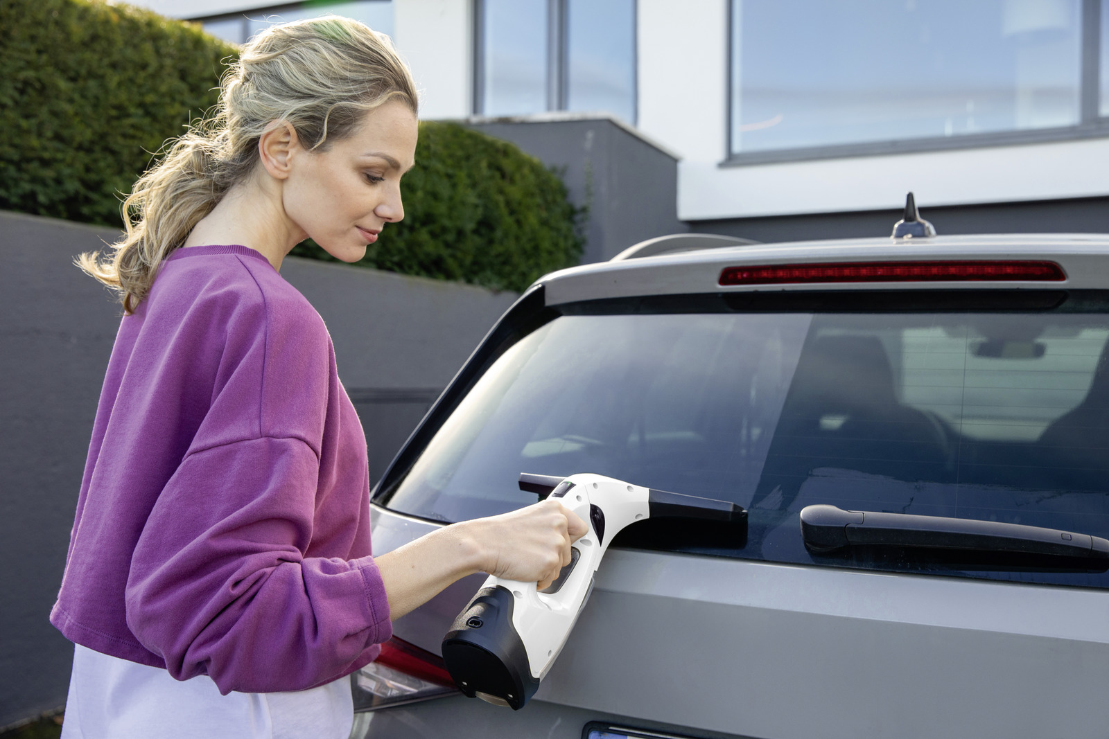 Kobieta czyści szybę samochodu czyścikiem. Na zewnątrz, słoneczny dzień.