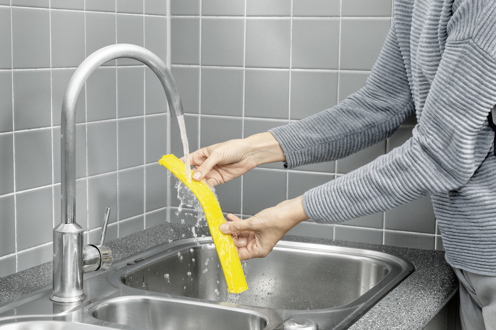A person washes a yellow object under running water in a sink.