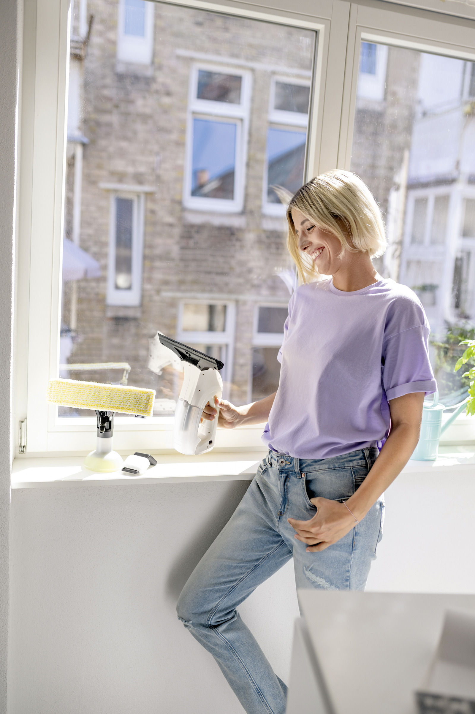 Une femme aux cheveux blonds nettoie une fenêtre avec un aspirateur de vitres Kärcher.