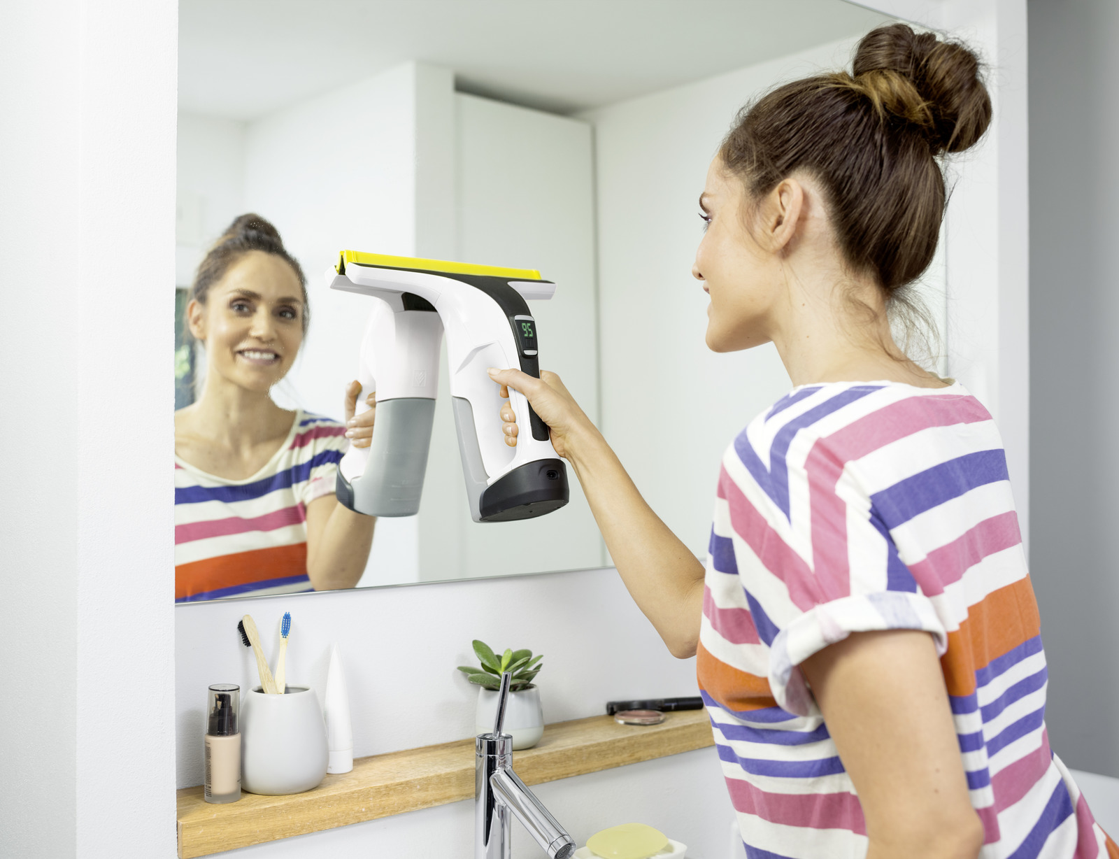 Woman cleans mirror with window cleaner. She wears a striped t-shirt.