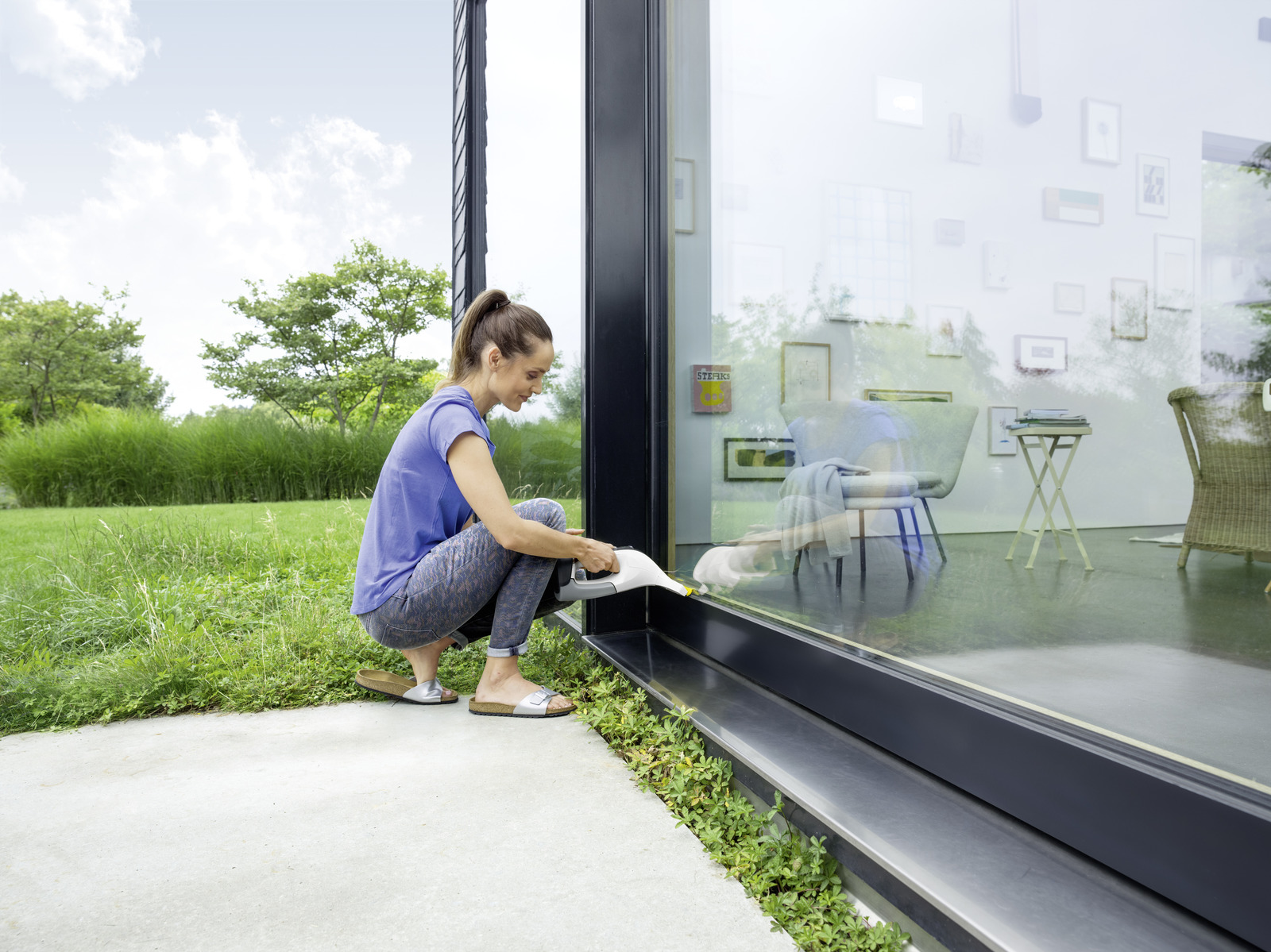 Woman cleaning window with a device, garden outside.