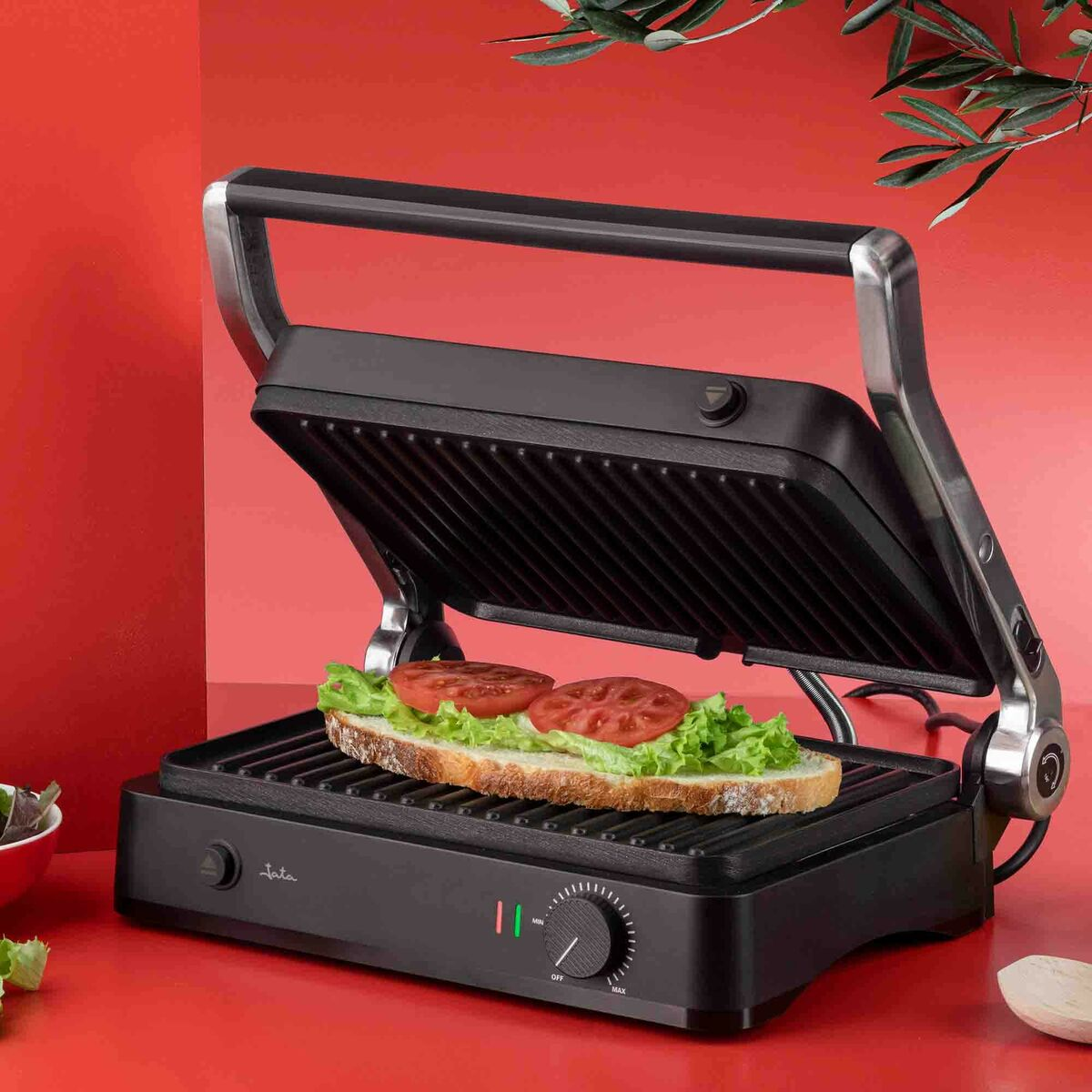 Una sandwichera abierta con un sándwich de lechuga y tomate en la parrilla.