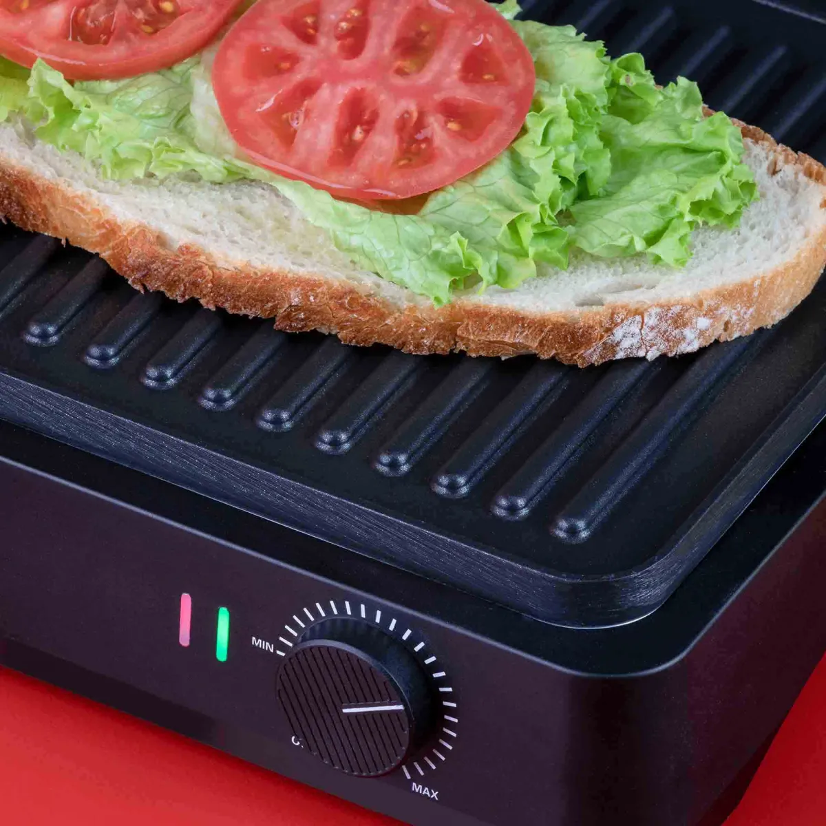 Un sándwich con lechuga y tomate en una parrilla. Fondo rojo.