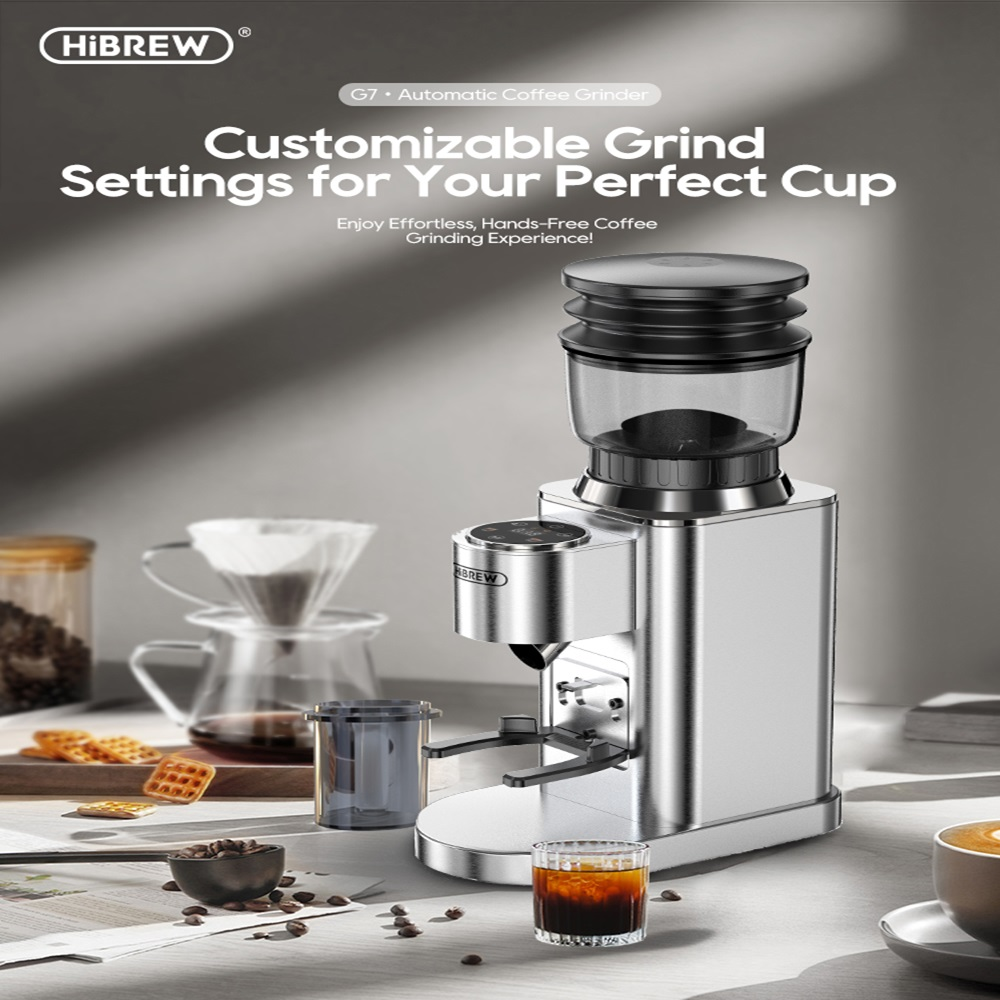 Molinillo de café automático plateado con tolva de vidrio, granos y vaso de café.