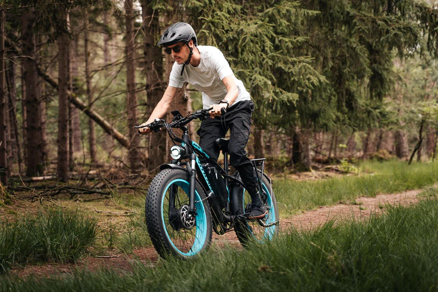 Un uomo guida una e-bike su un sentiero forestale, circondato da alberi.