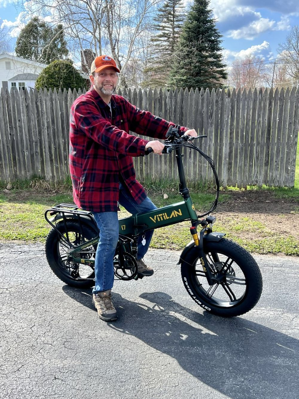 Un uomo su una e-bike verde siede su una strada asfaltata davanti a una recinzione di legno.