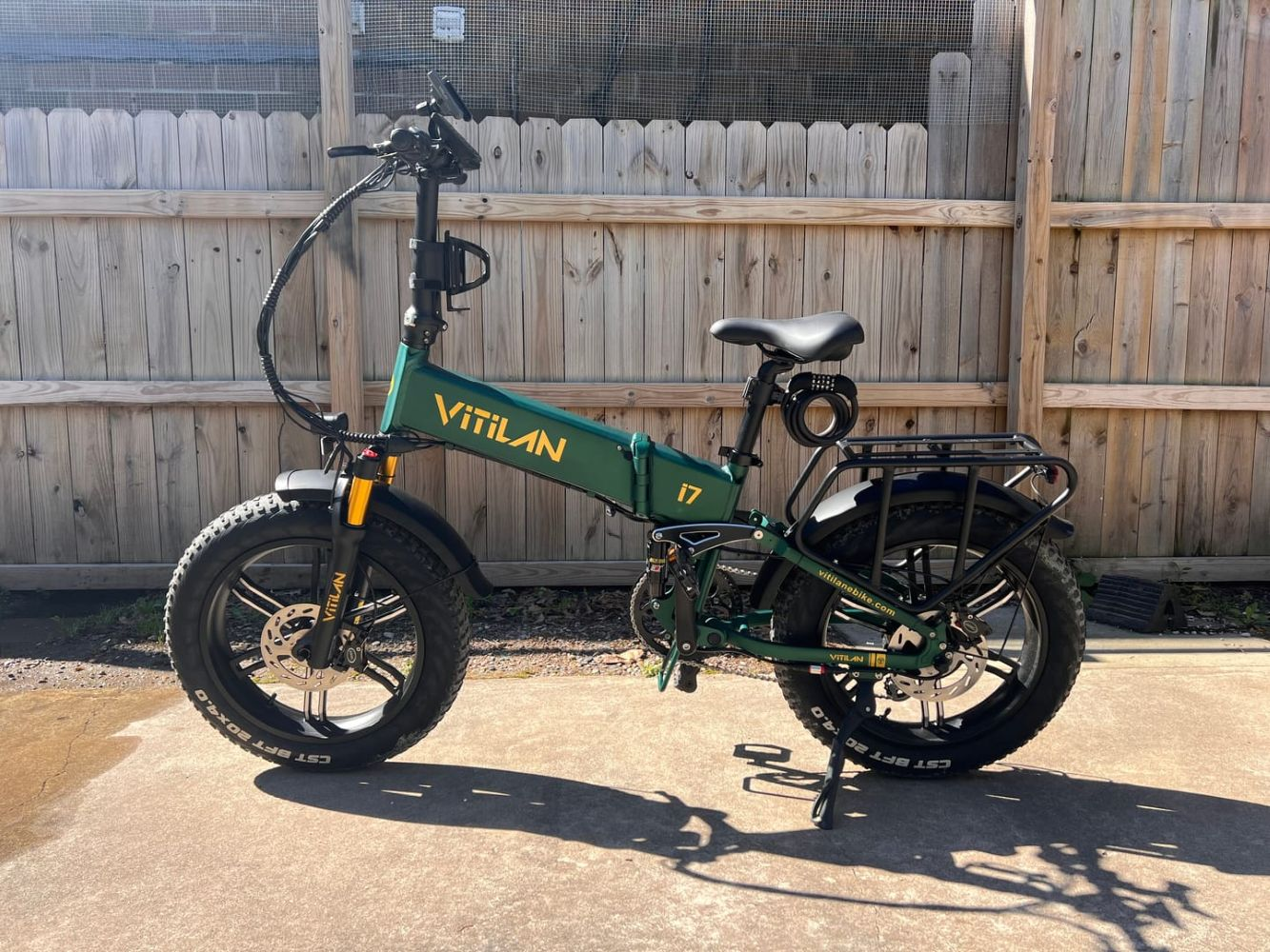 Una bici elettrica pieghevole verde si trova su un sentiero di cemento davanti a una recinzione di legno.