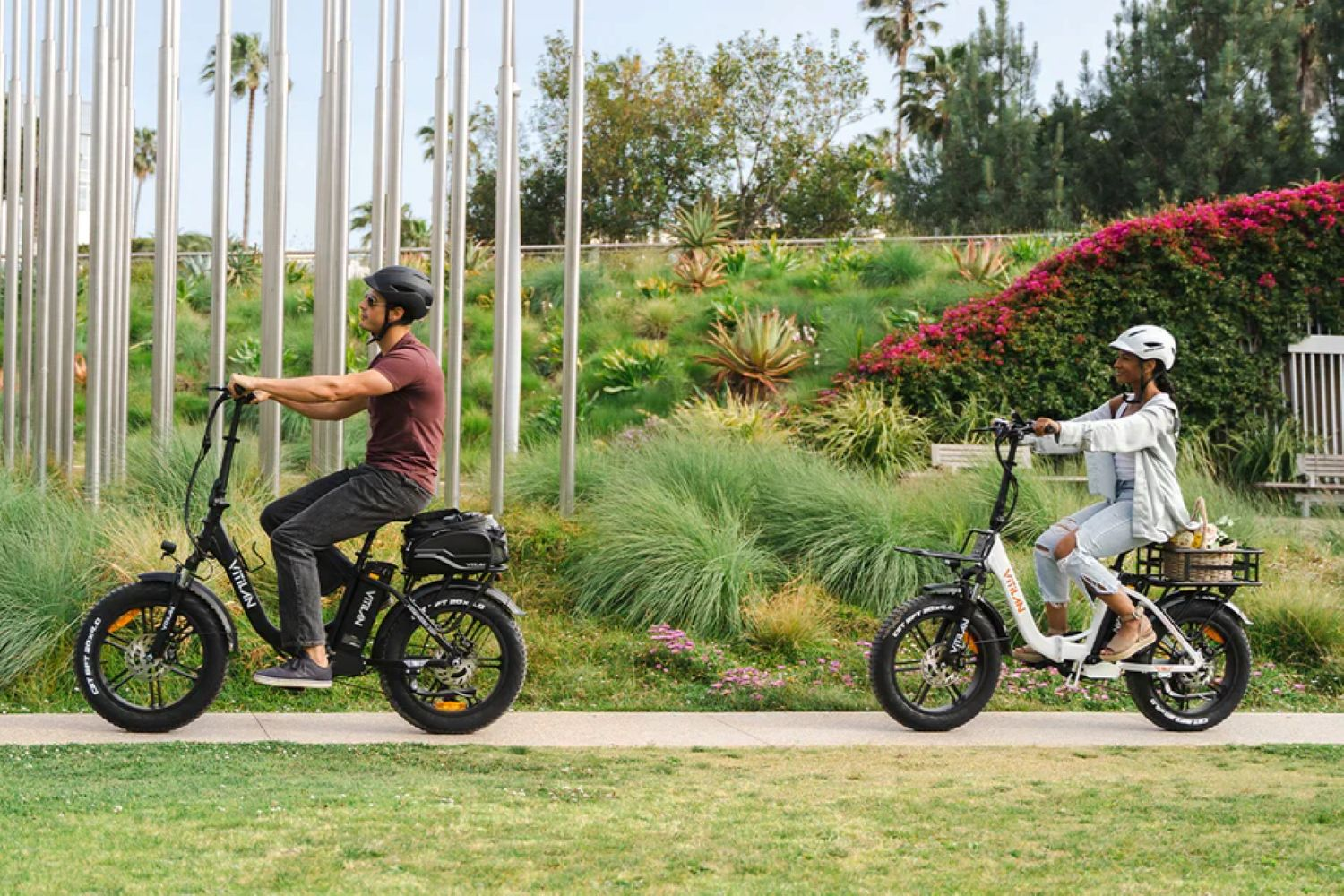 Due persone su e-bike in un parco con fogliame verde lussureggiante e alberi.
