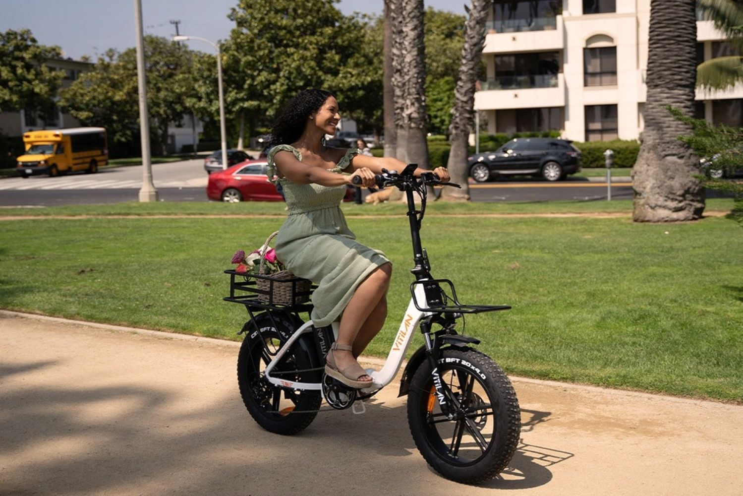 Una donna guida una e-bike con fiori nel cestino su un sentiero soleggiato.