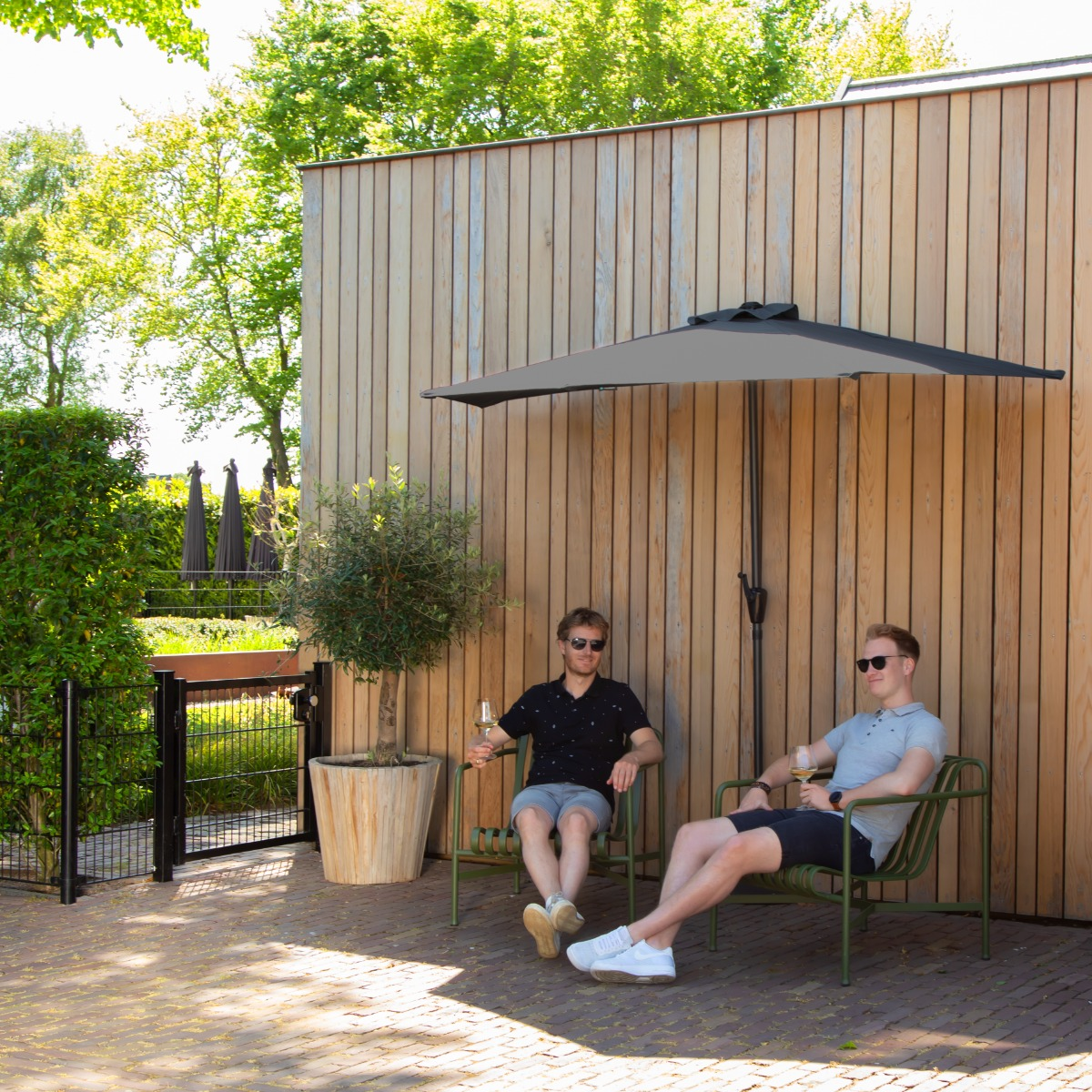 Twee mannen zitten buiten onder een parasol op groene stoelen.