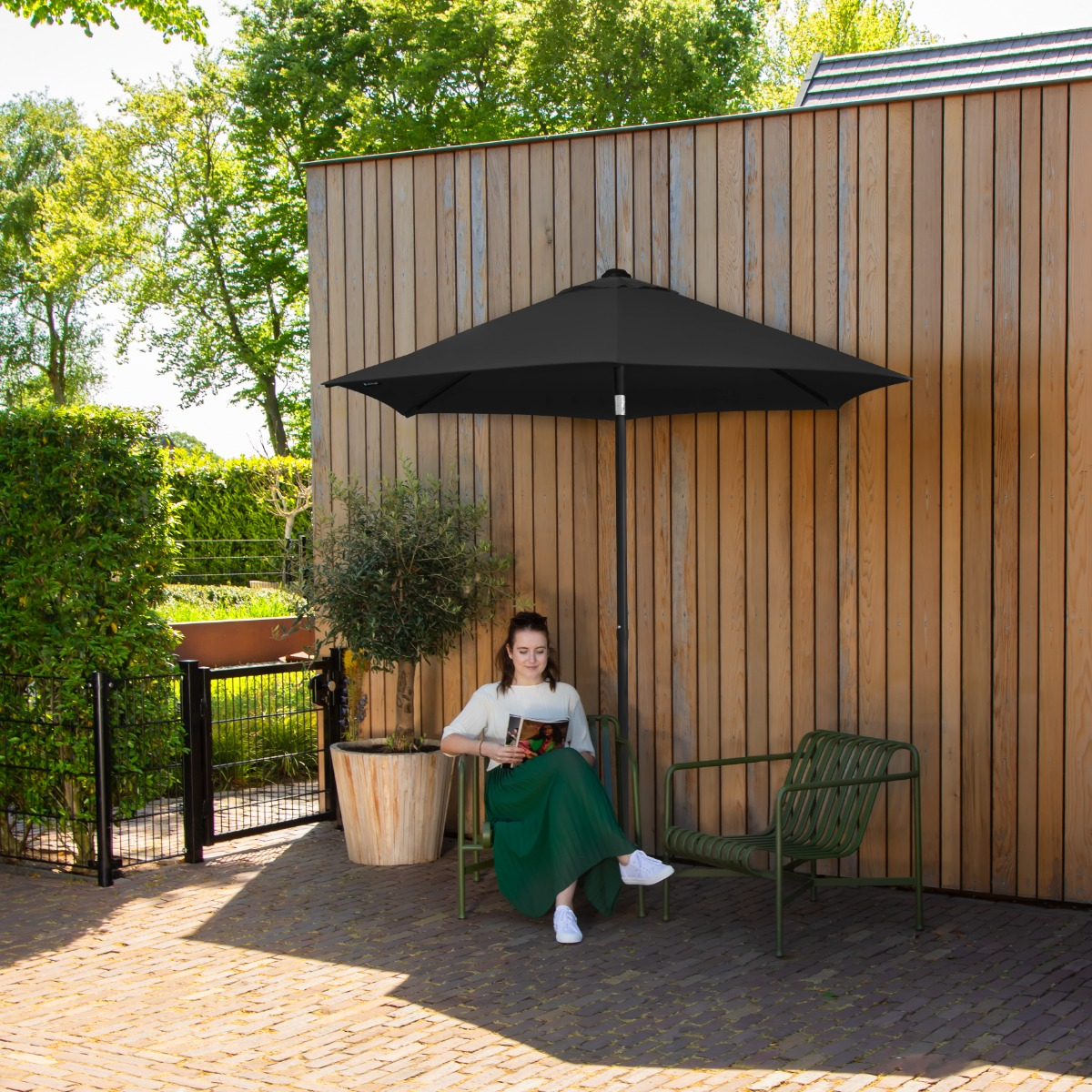 Een vrouw zit onder een zwarte parasol een tijdschrift te lezen.
