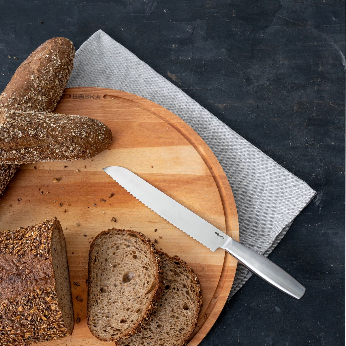 Breads on a wooden board with a bread knife and a gray cloth.