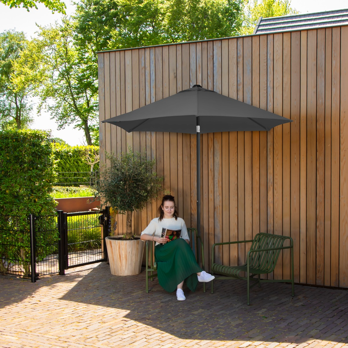 Vrouw leest boek onder parasol bij houten muur met olijfboom.