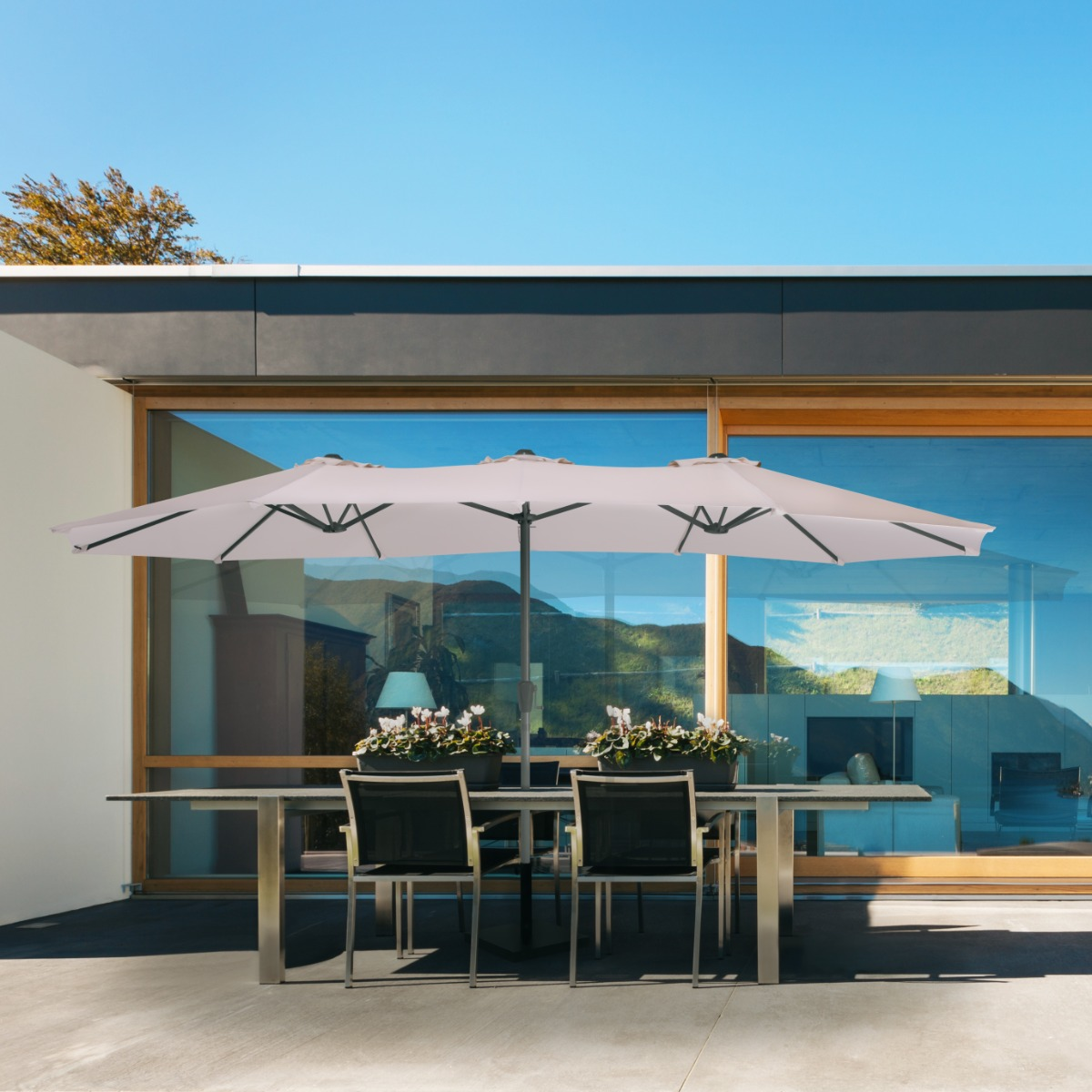 Een grote, lichtgekleurde parasol bedekt een tafel met vier stoelen en planten.