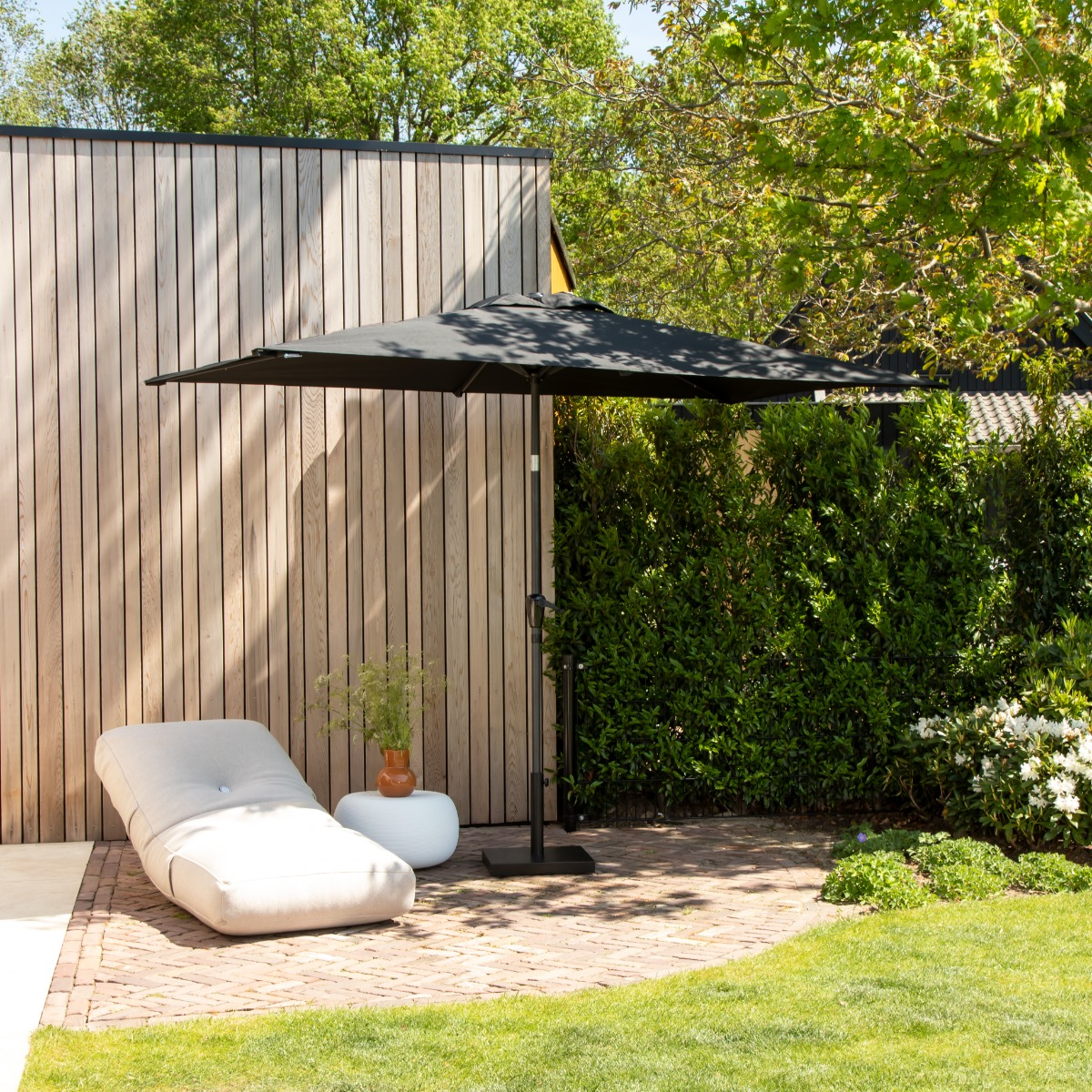 Een moderne tuin met ligstoel, parasol en houten wand.