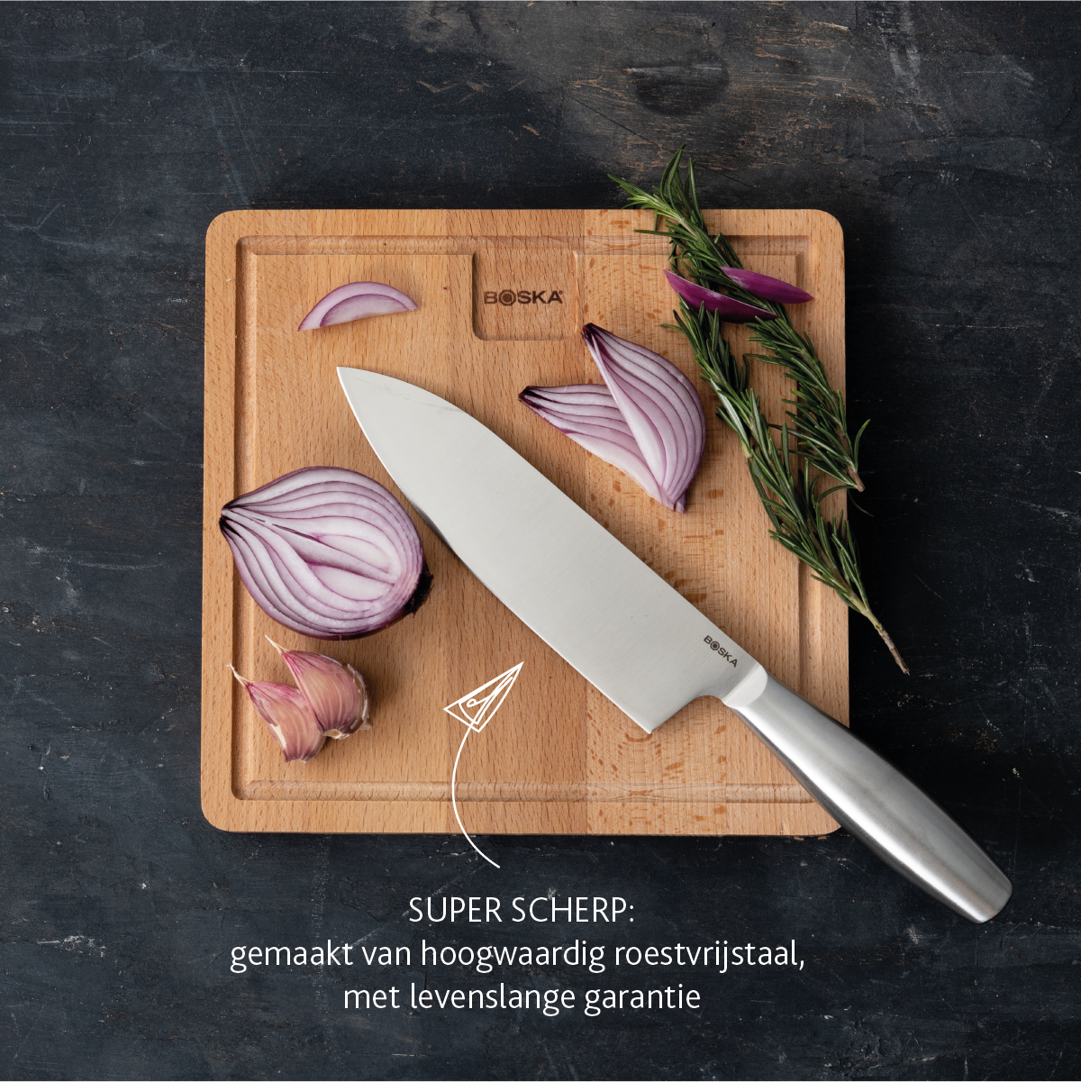 A chef's knife rests on a wooden board next to red onions and rosemary.