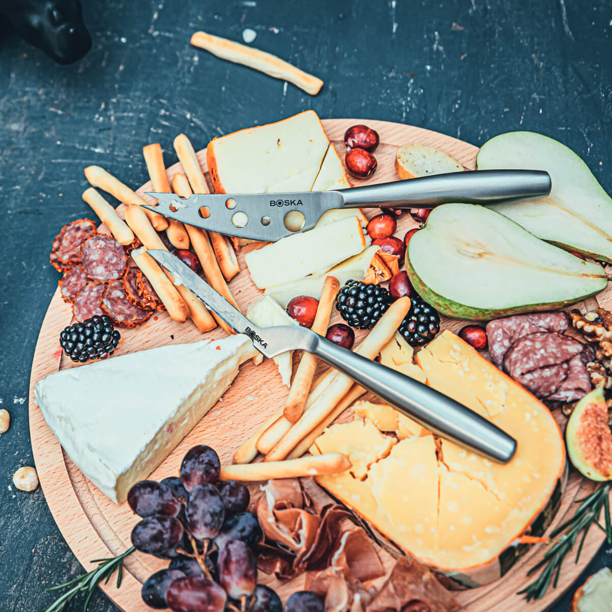 Cheese board with grapes, berries, pears, salami, and breadsticks.