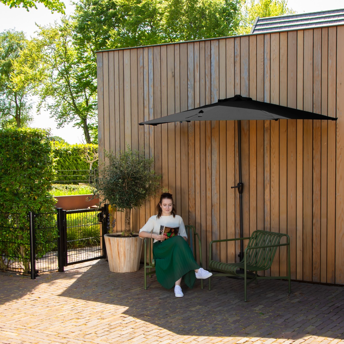 Een vrouw leest een boek op een groene bank voor een houten muur.