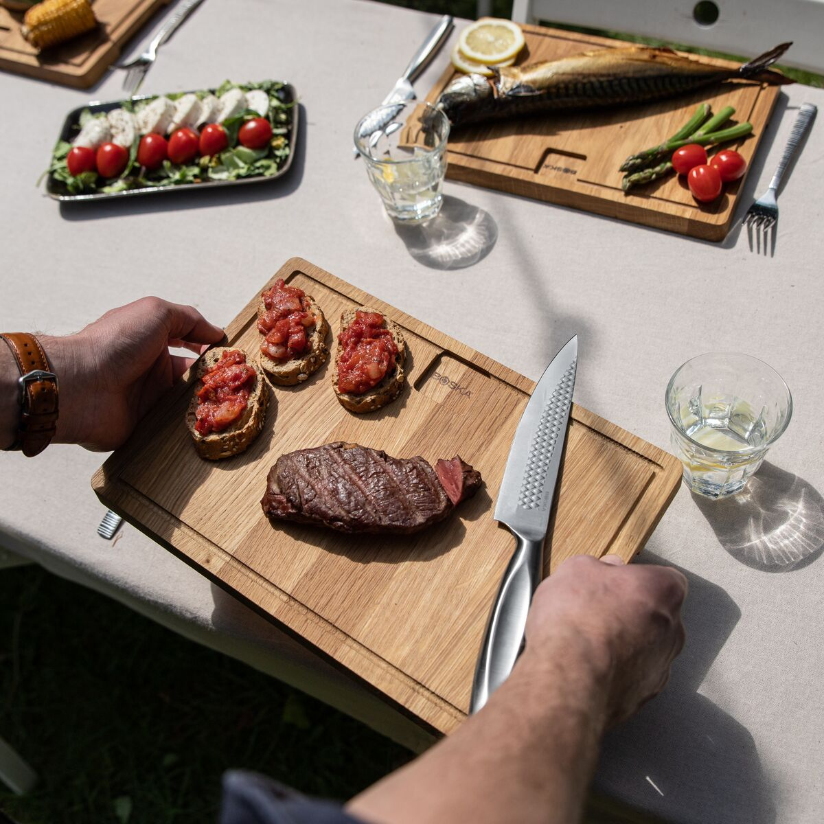 A man places a bread slice with tomatoes onto a board next to a steak.