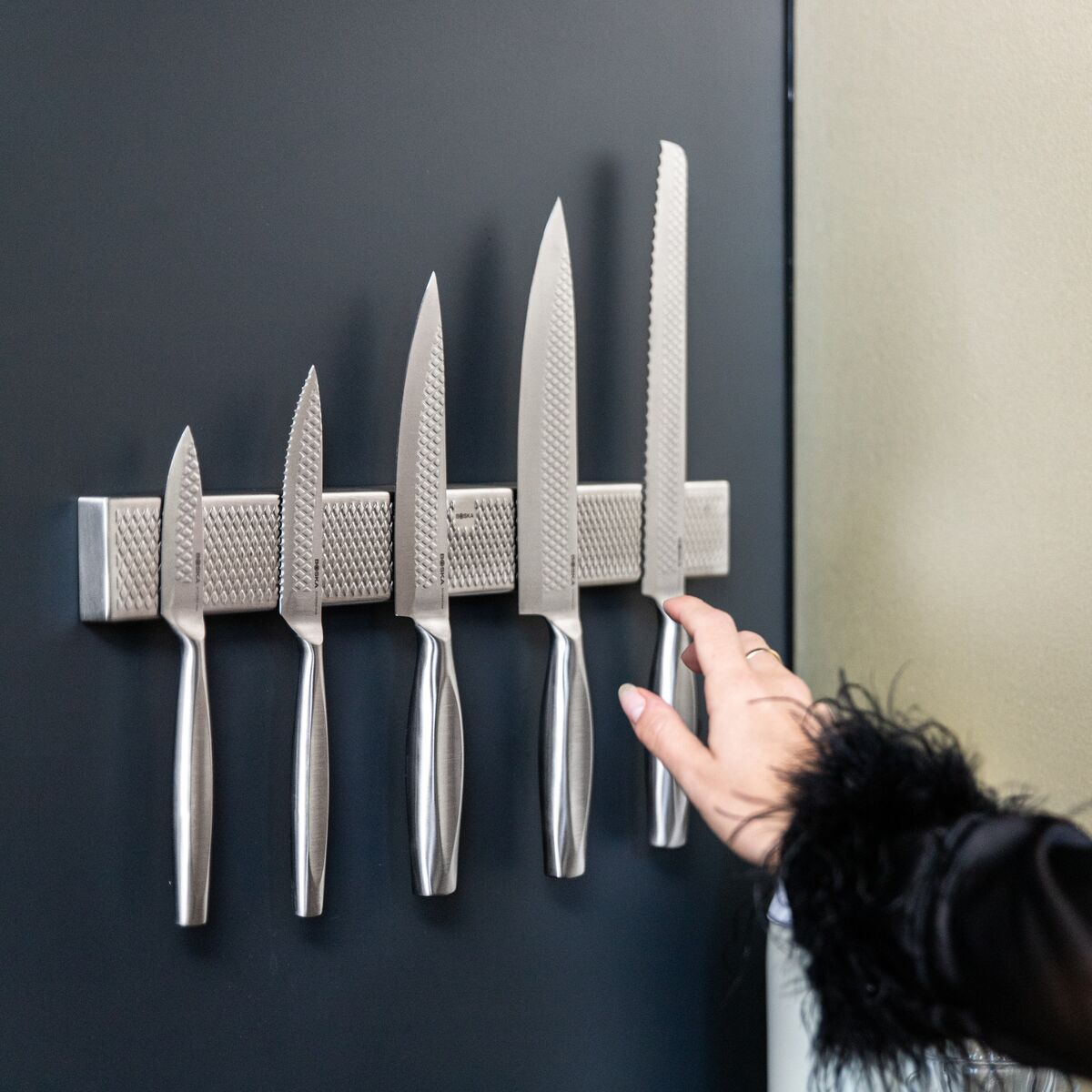 Five knife blades on a magnetic strip, a hand reaches for the last one.
