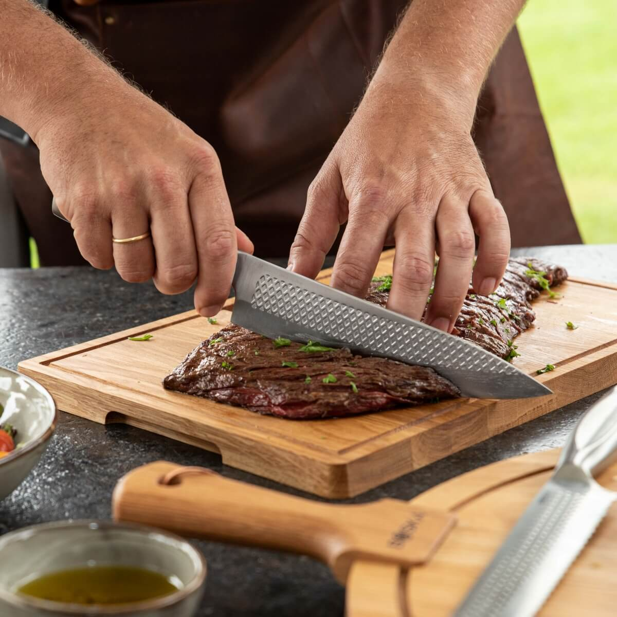 Hands slicing grilled steak on a wooden board with a knife, garnished with parsley.