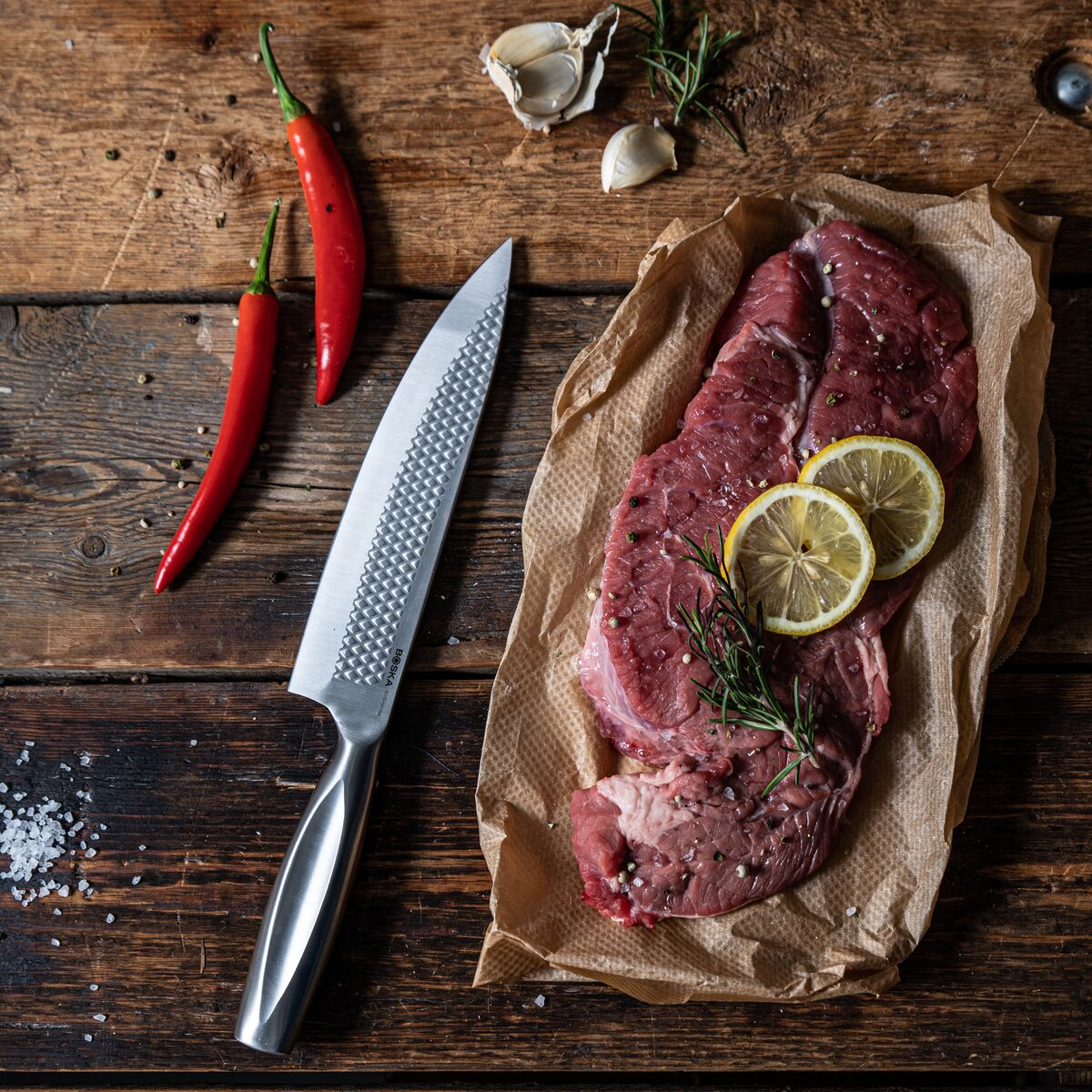 Raw steak with lemon slices, chilies, garlic and knife on wood.