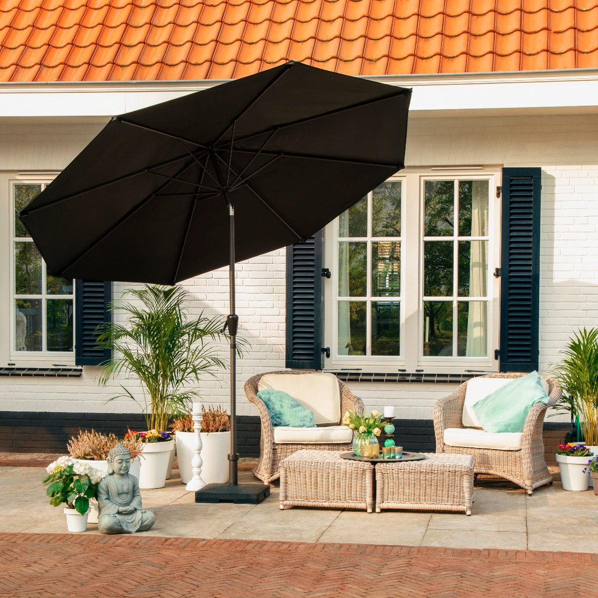 Terras met rieten stoelen, salontafel, Boeddhabeeld en zwarte parasol.