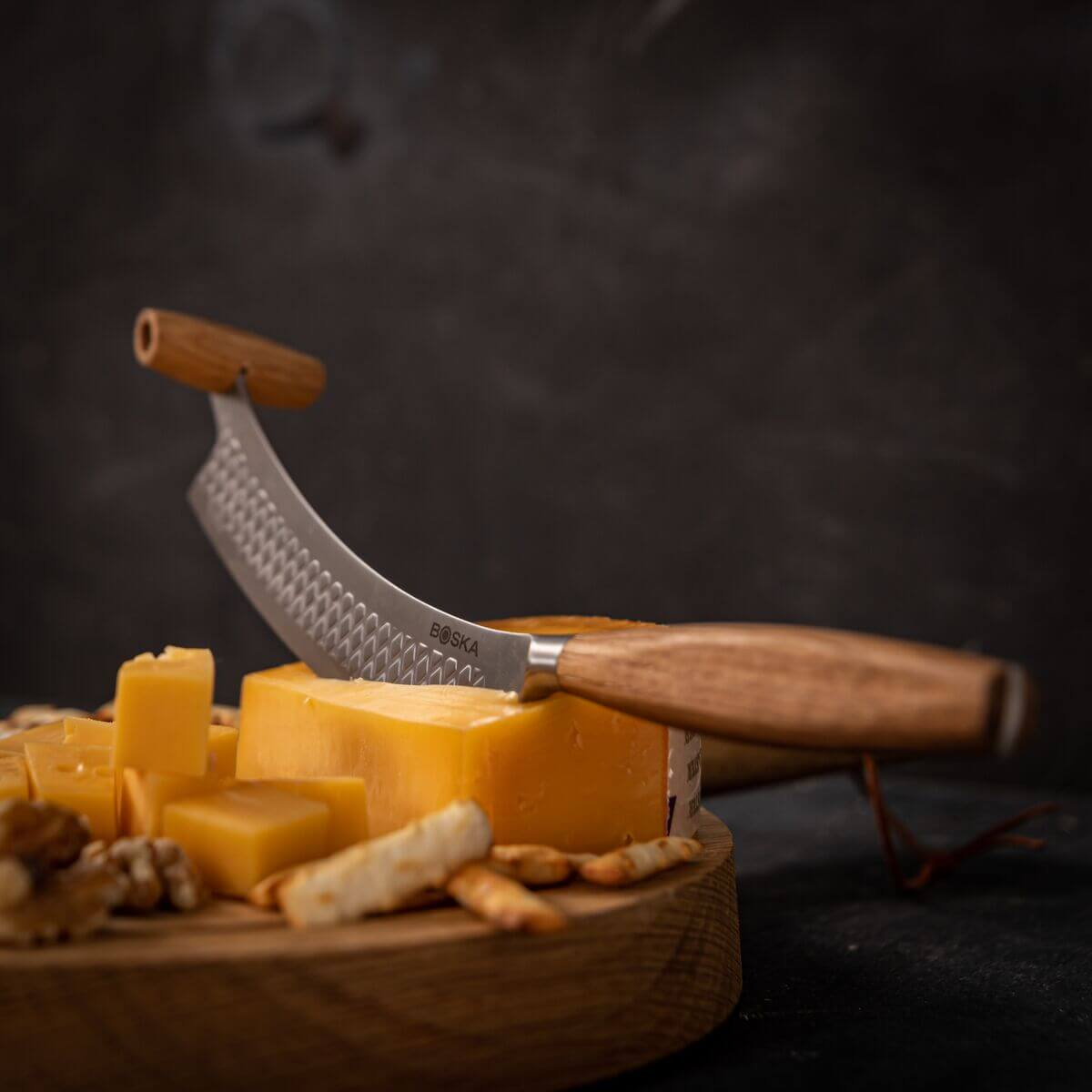 Cheese knife with wooden handle on a wooden board with cheese and crackers.