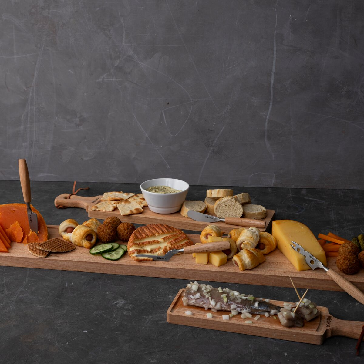 A wooden board with cheese, crackers, bread, sausages, and a fish dish.