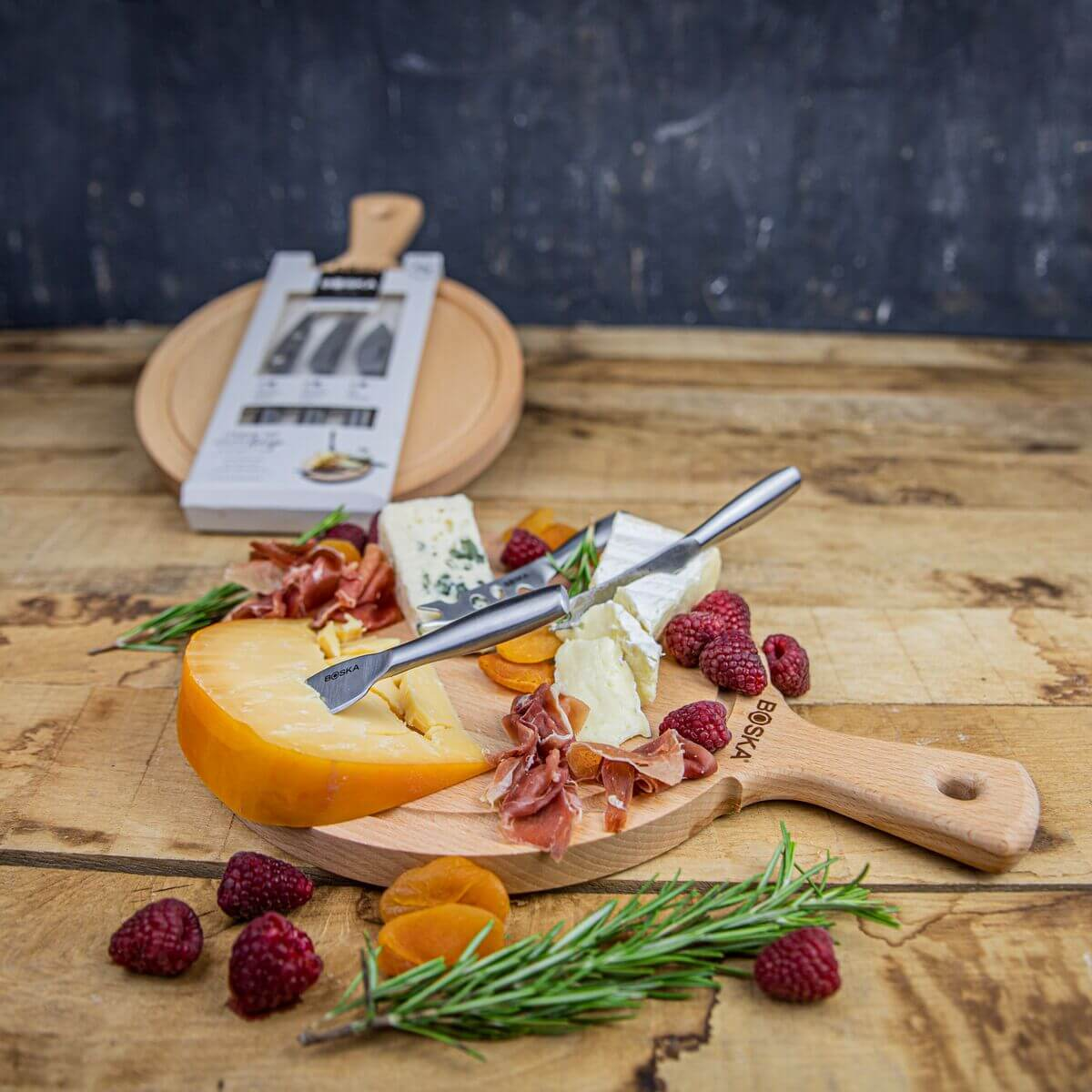Cheese board with various cheeses, ham, berries, and herbs.