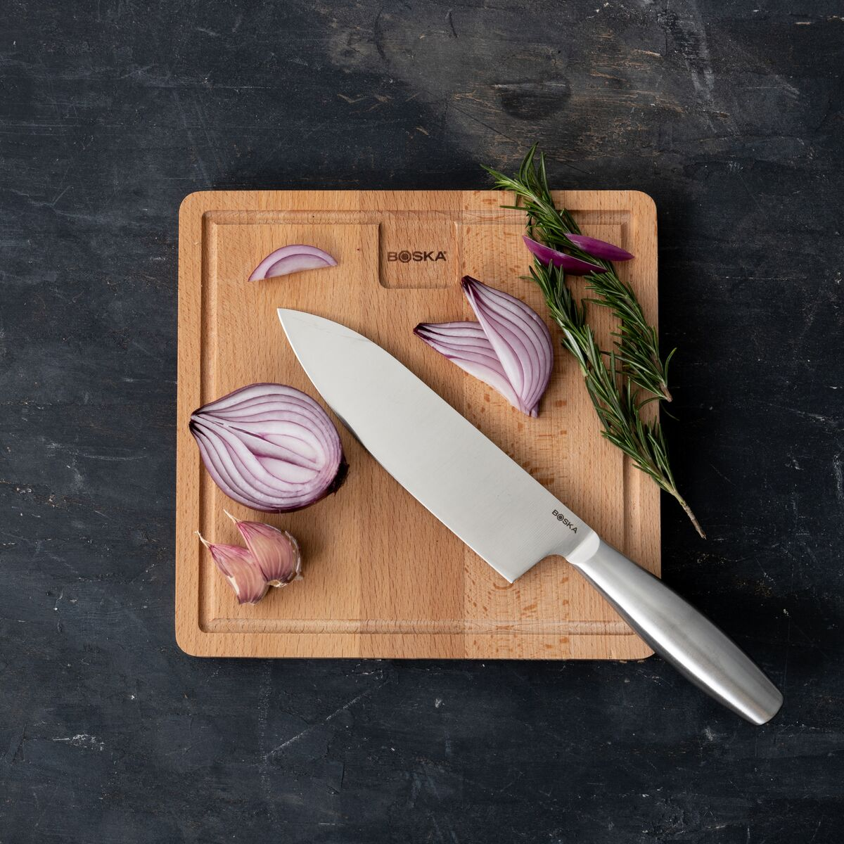 A kitchen knife lies on a wooden cutting board next to onions and garlic.