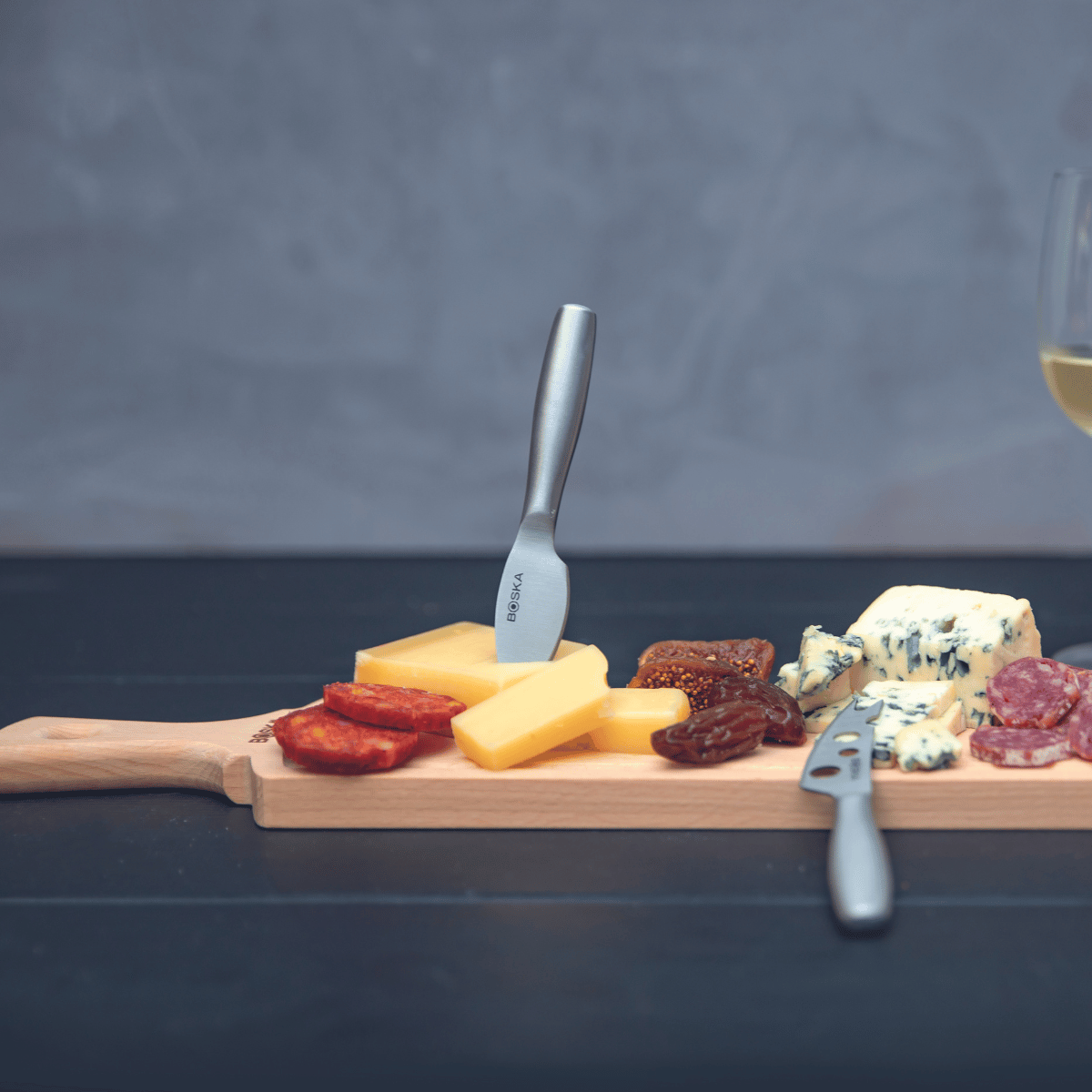 A cheese board with various cheeses, sausage, figs, and a glass of wine.
