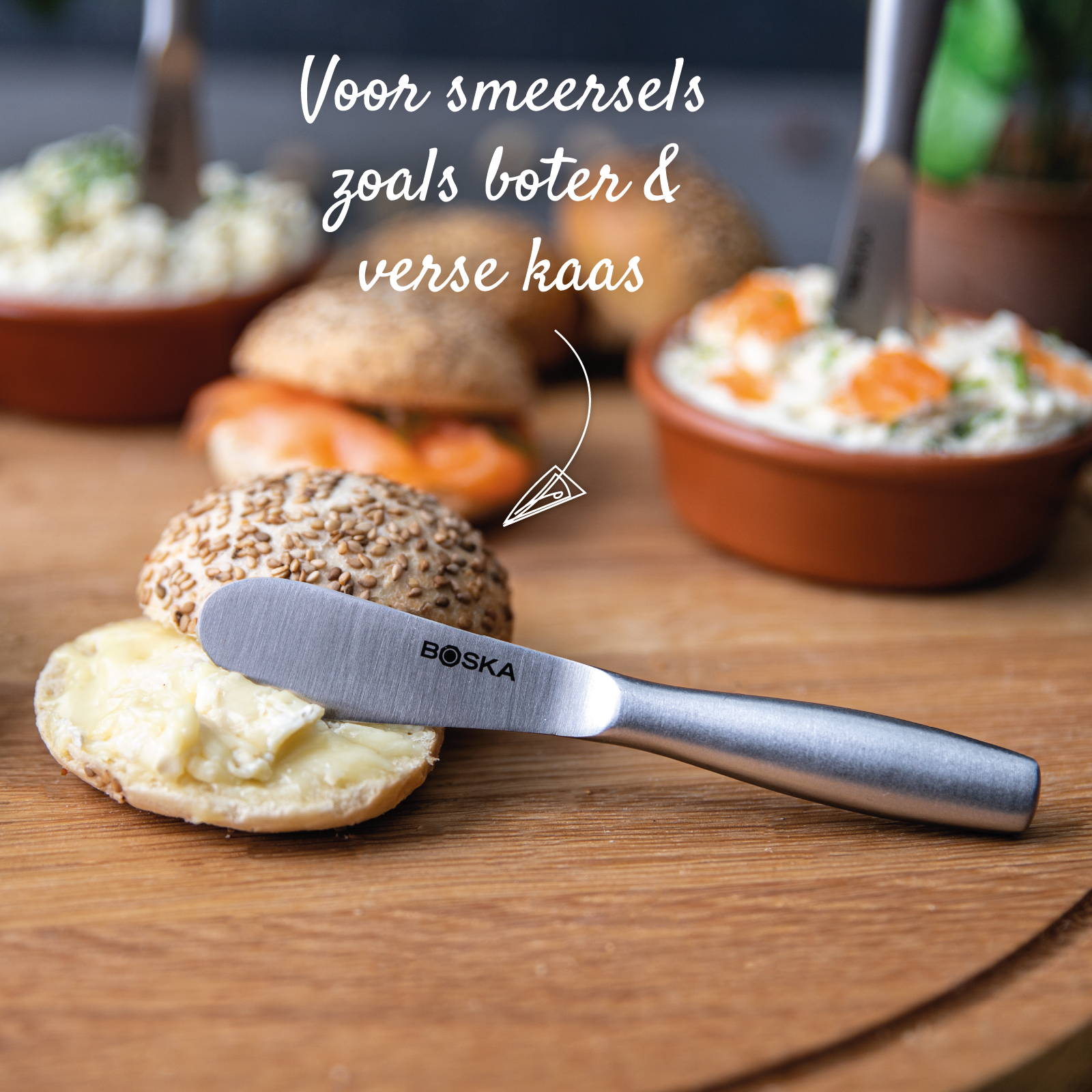 A butter knife spreading butter on a bun, with other buns and dips in the background.