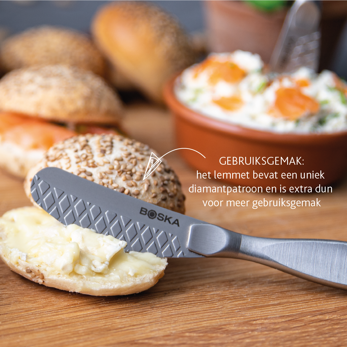 A knife with a diamond pattern spreads butter on a bun.