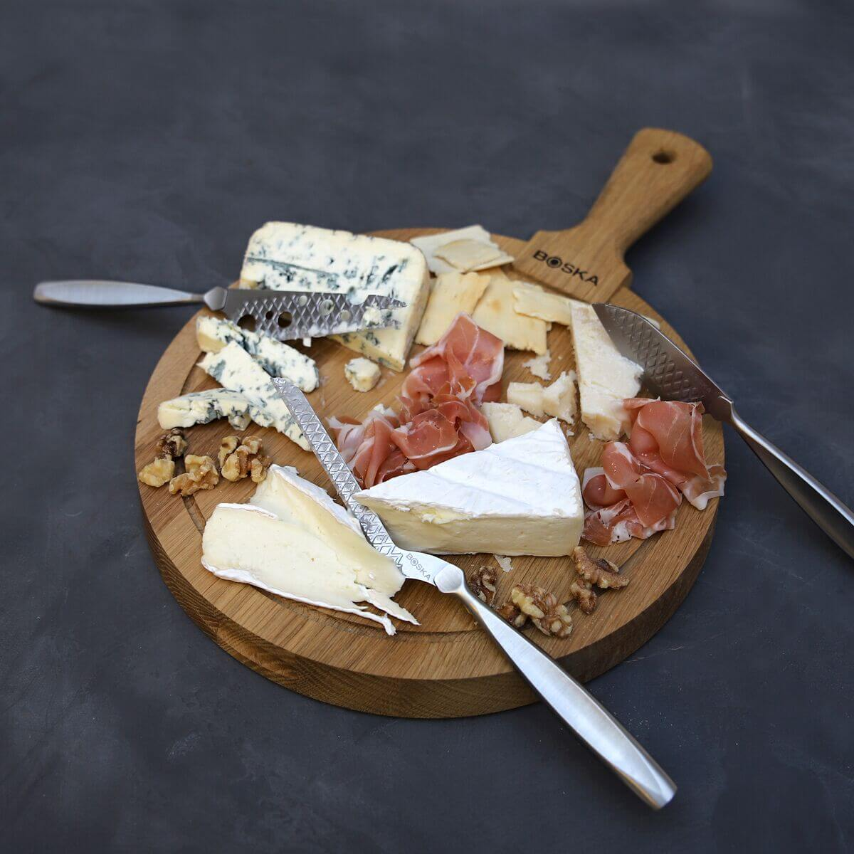 Cheese board with assorted cheeses, prosciutto, walnuts, and crackers on a wooden board.