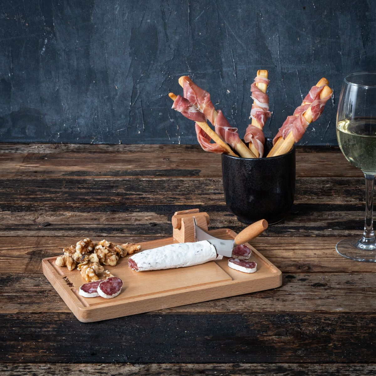 Breadsticks wrapped in ham, cheese, nuts and sausage on a wooden board with wine.