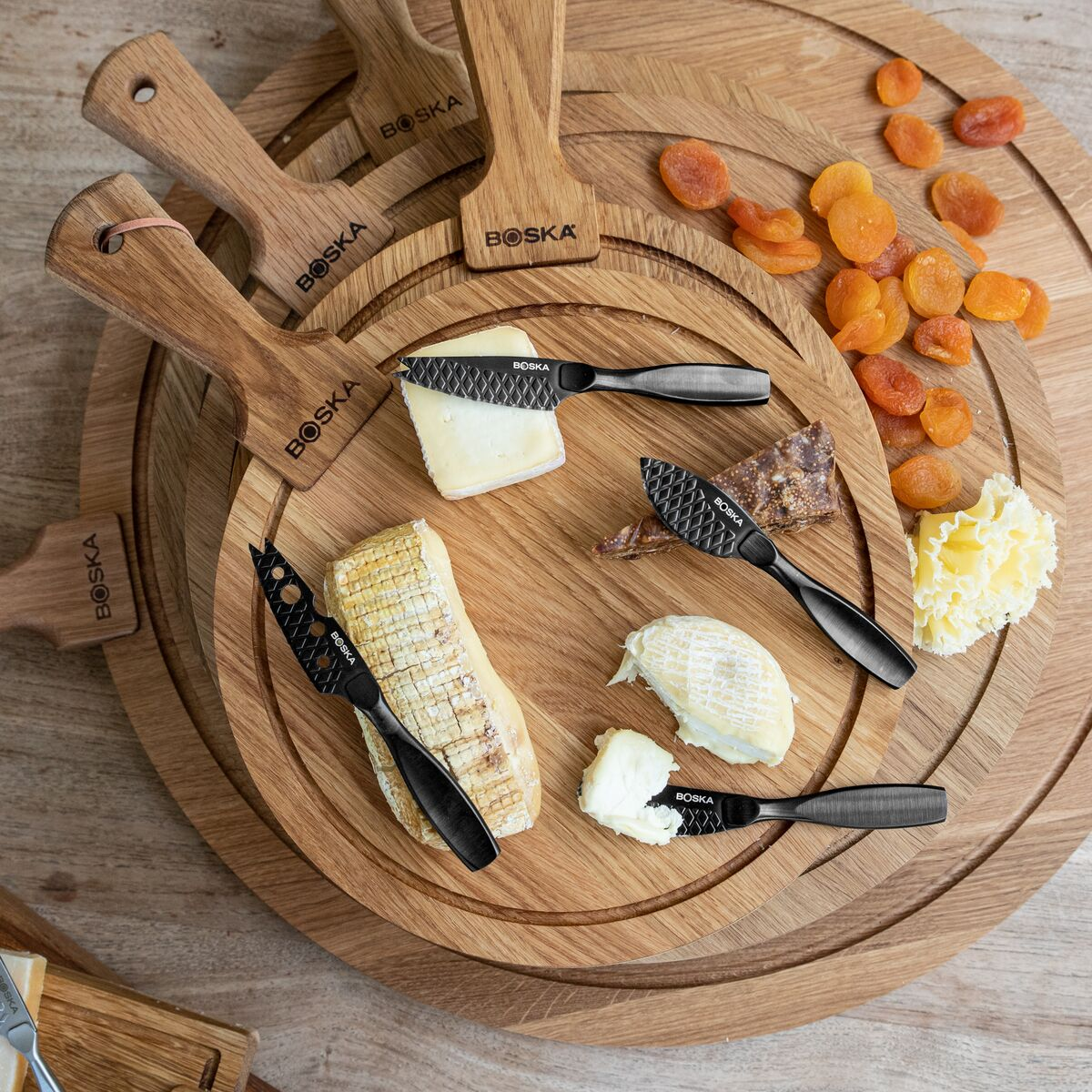 A cheese board featuring assorted cheeses, knives, and dried apricots.