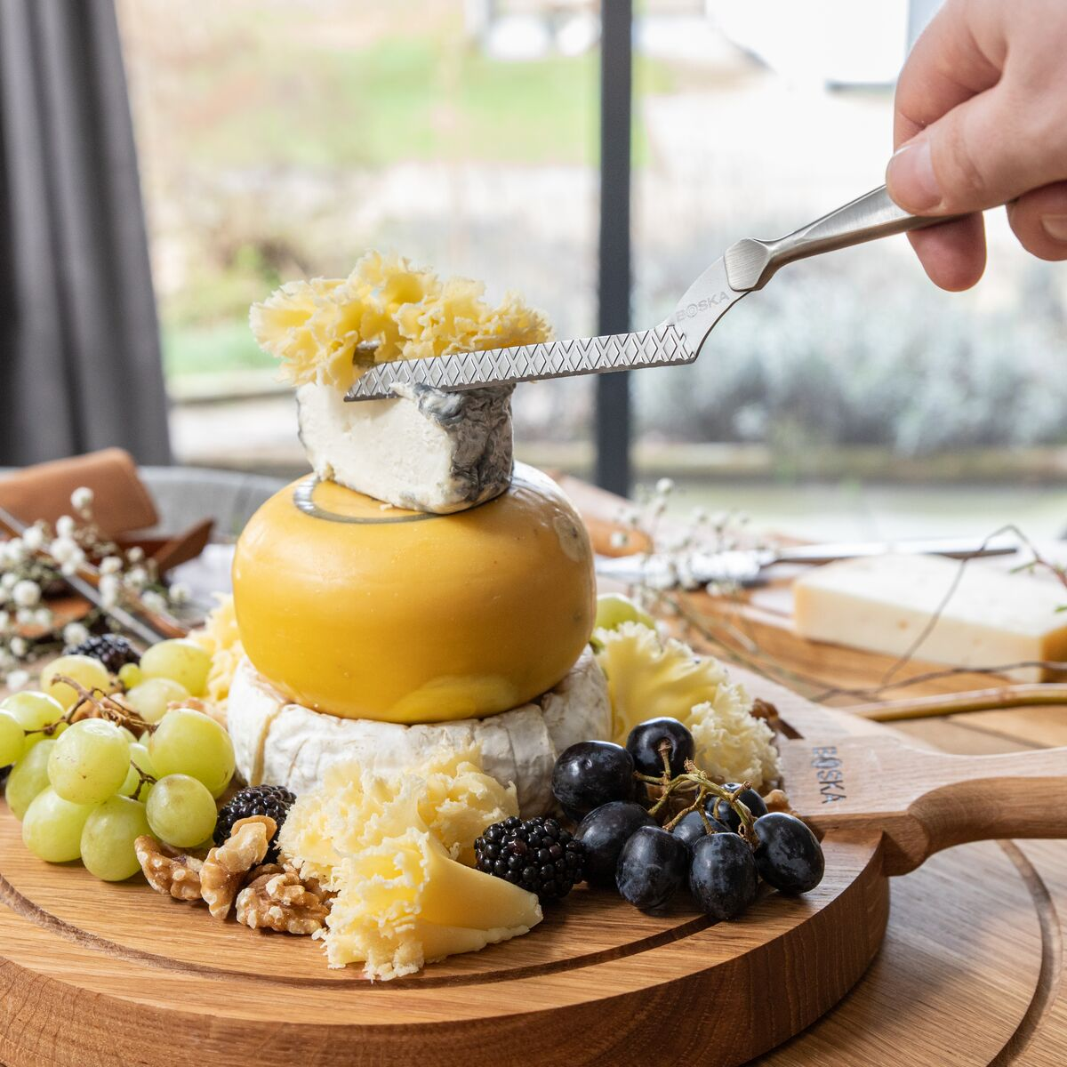 Cheese platter with grapes, berries, and nuts; cheese knife in use.