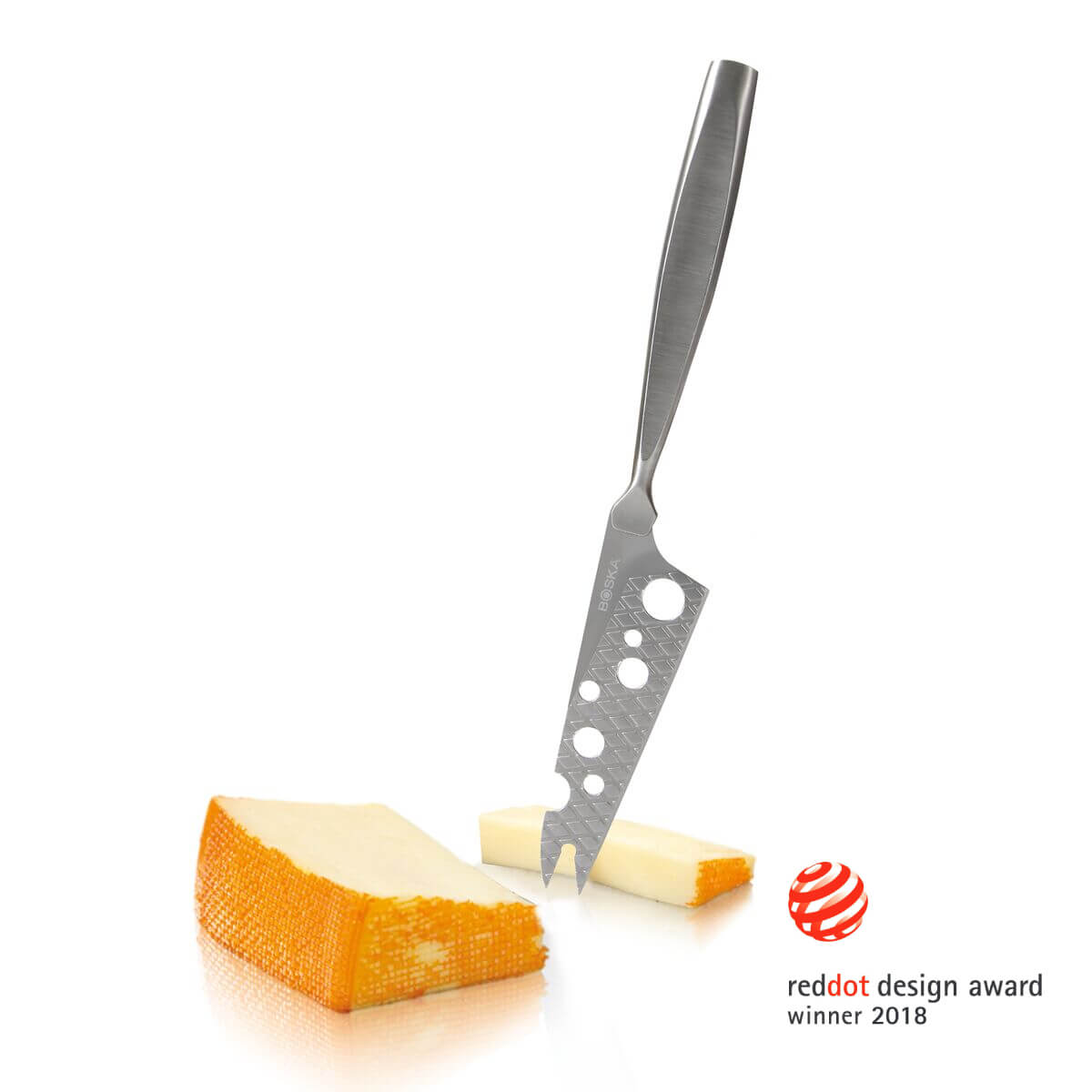 Cheese knife with holes in a piece of cheese, another piece next to it.