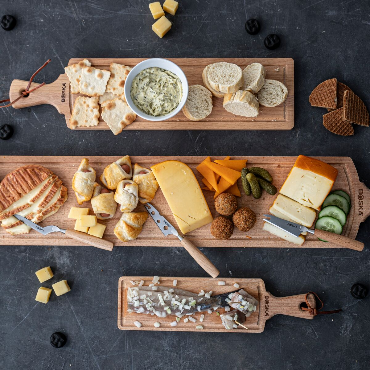 Cheese board with bread, crackers, dips, pigs in a blanket, and herring with onions.